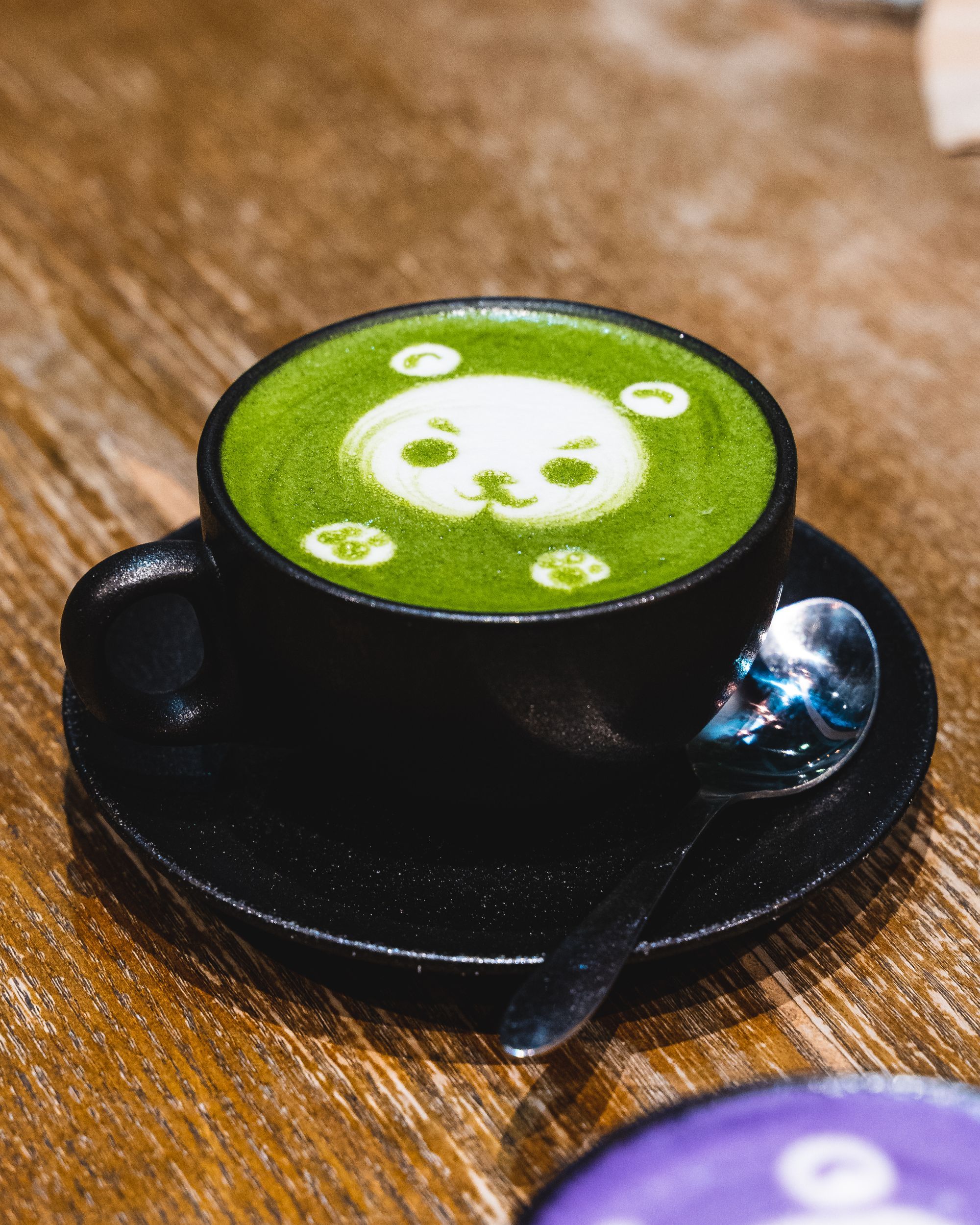 Close up of green tea latte in a black mug and on a black plate, with a teddy bear as latte art