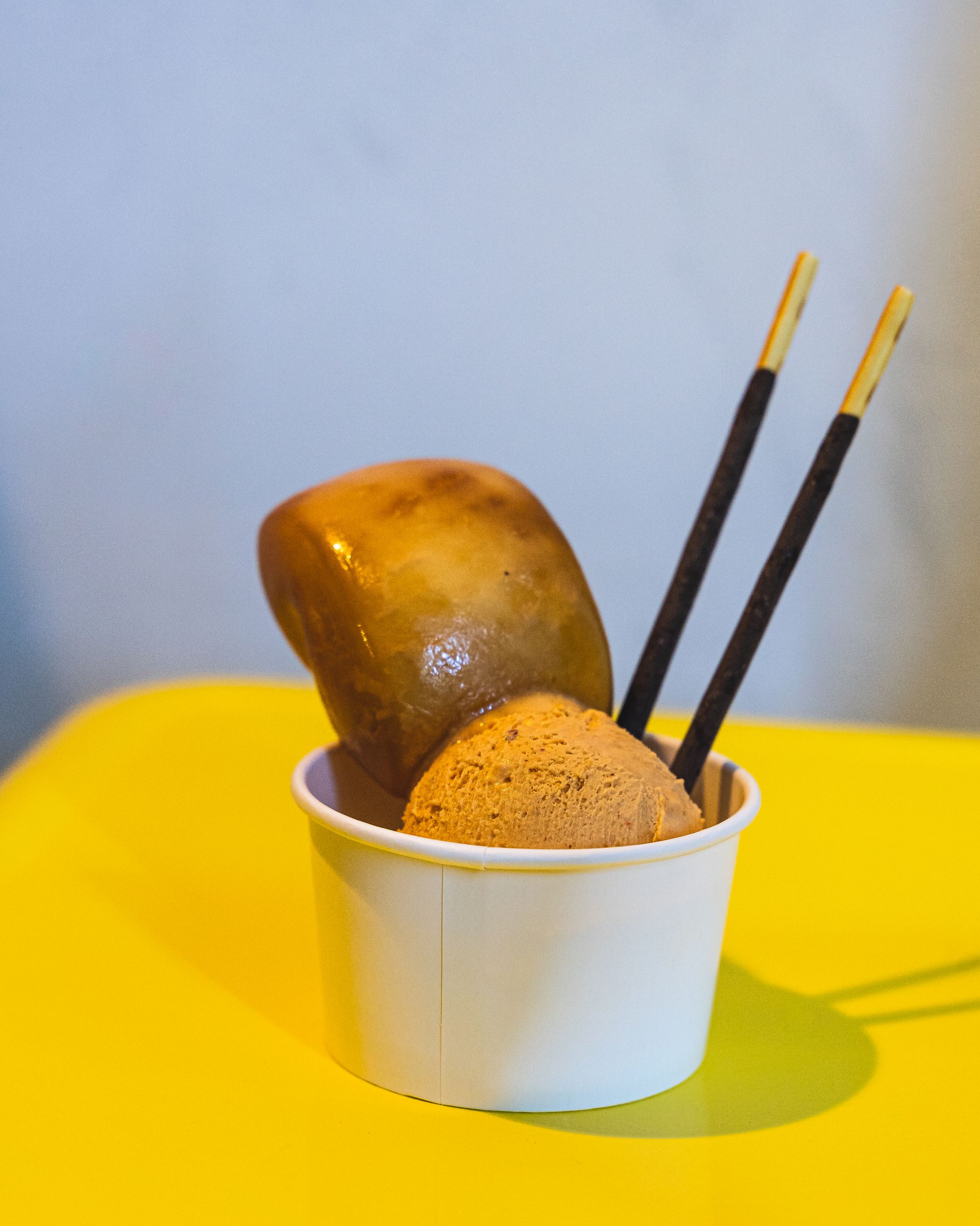 Gelato in a paper cup with two pocky sticks and a mantou as garnish