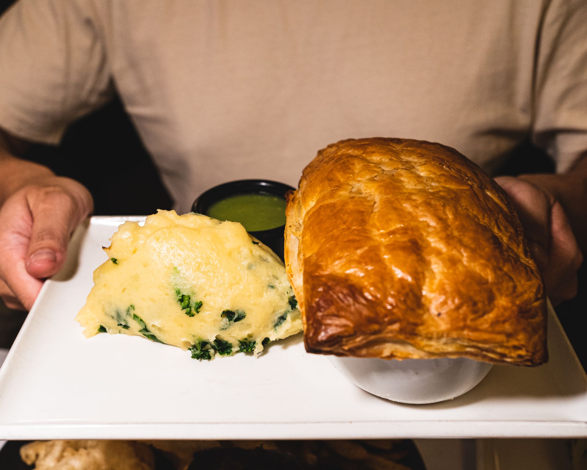 Hand holding a plate with mash potato and a pie