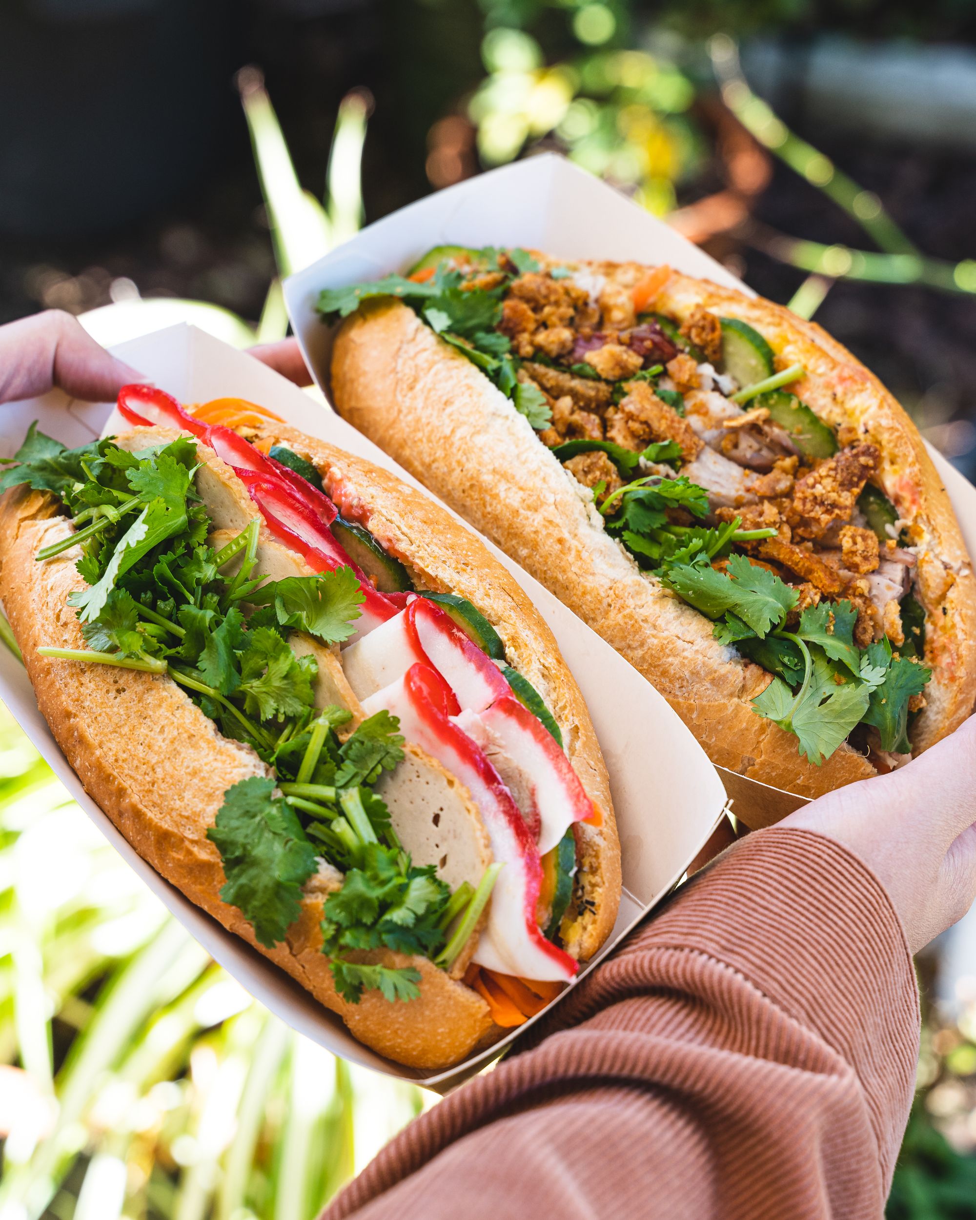 Close up shot of hands holding banh mi on paper trays