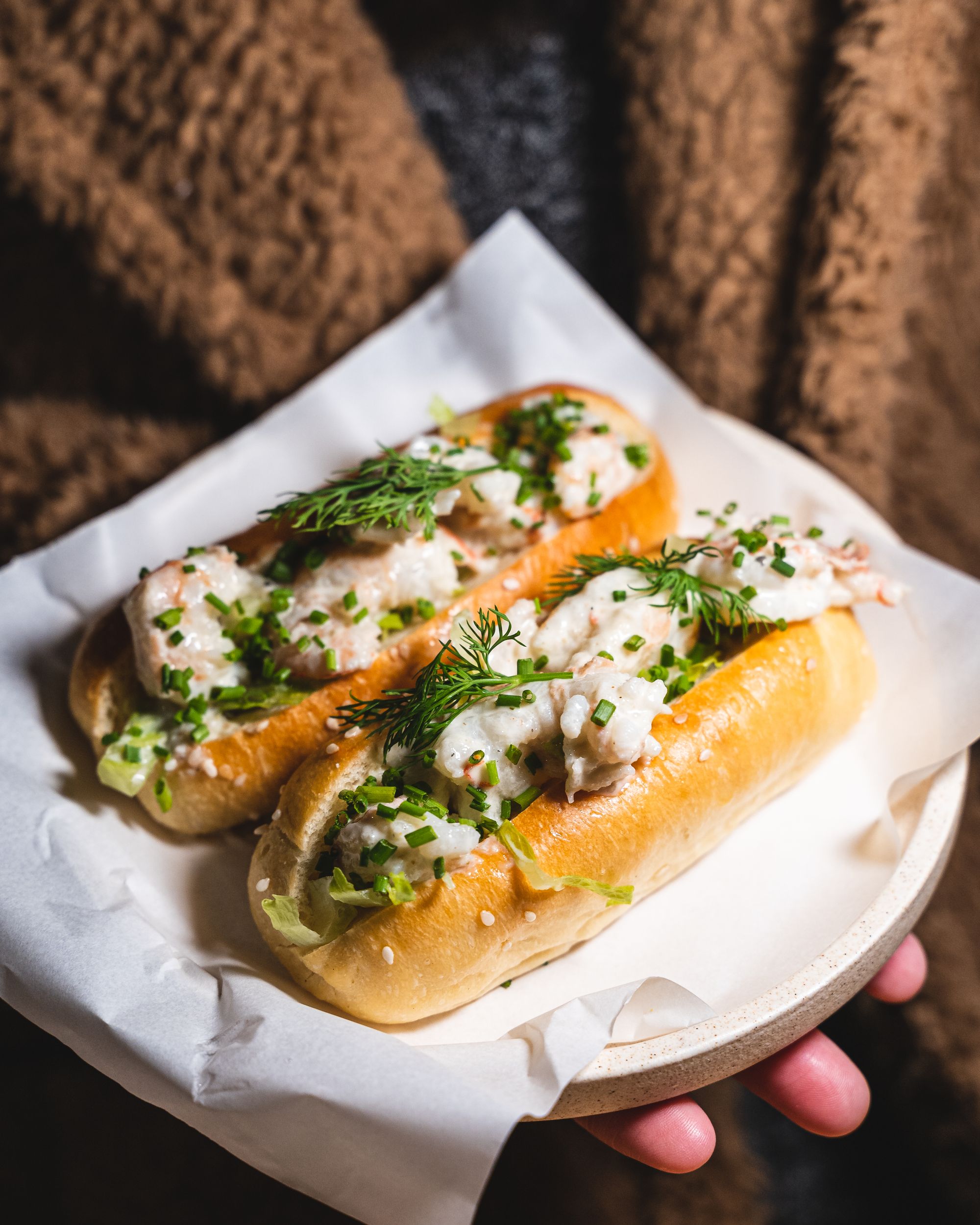 Close up of hand holding a plate with two prawn rolls