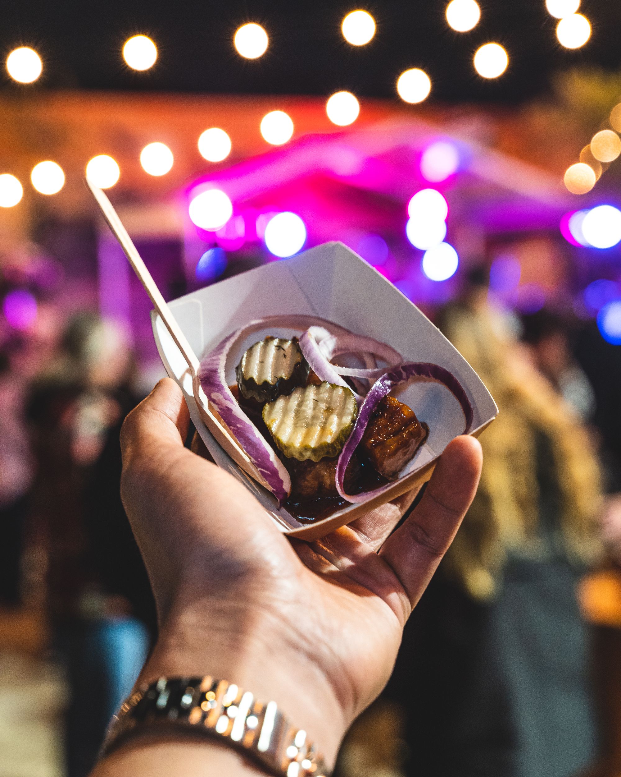 Hand holding a paper plate with pork belly