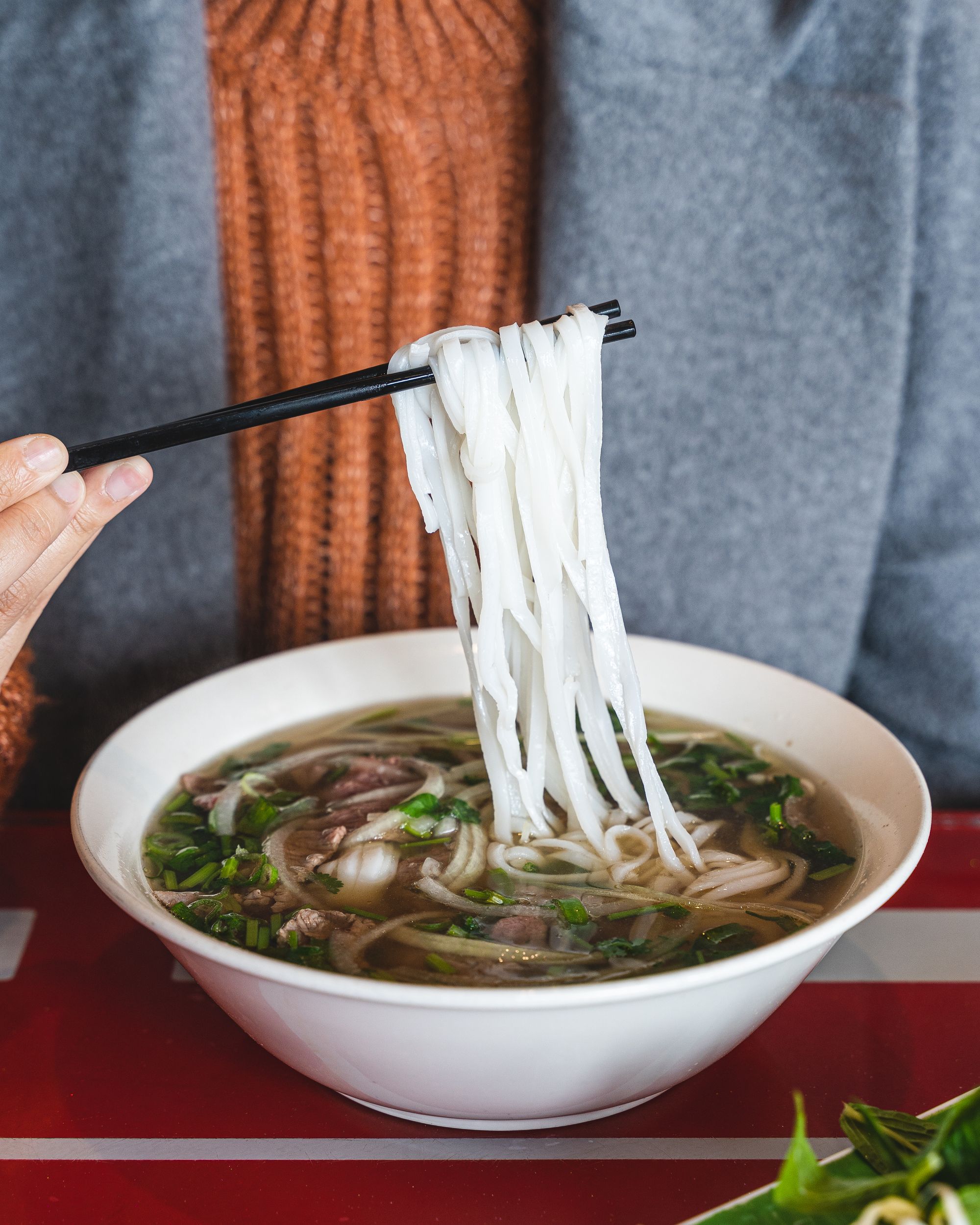 Close up of a bowl of pho with chopsticks lifting up some noodles