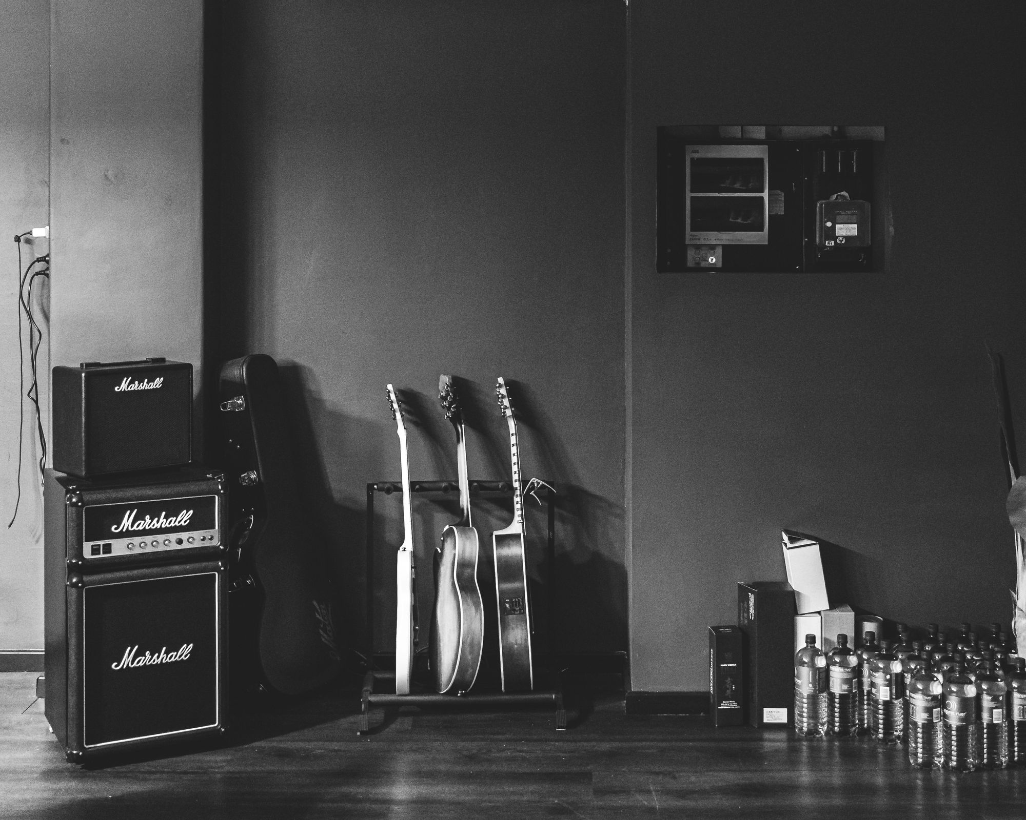 Black and white photo of a wall with Marshall guitar amps, guitars and water bottles lined up against wall