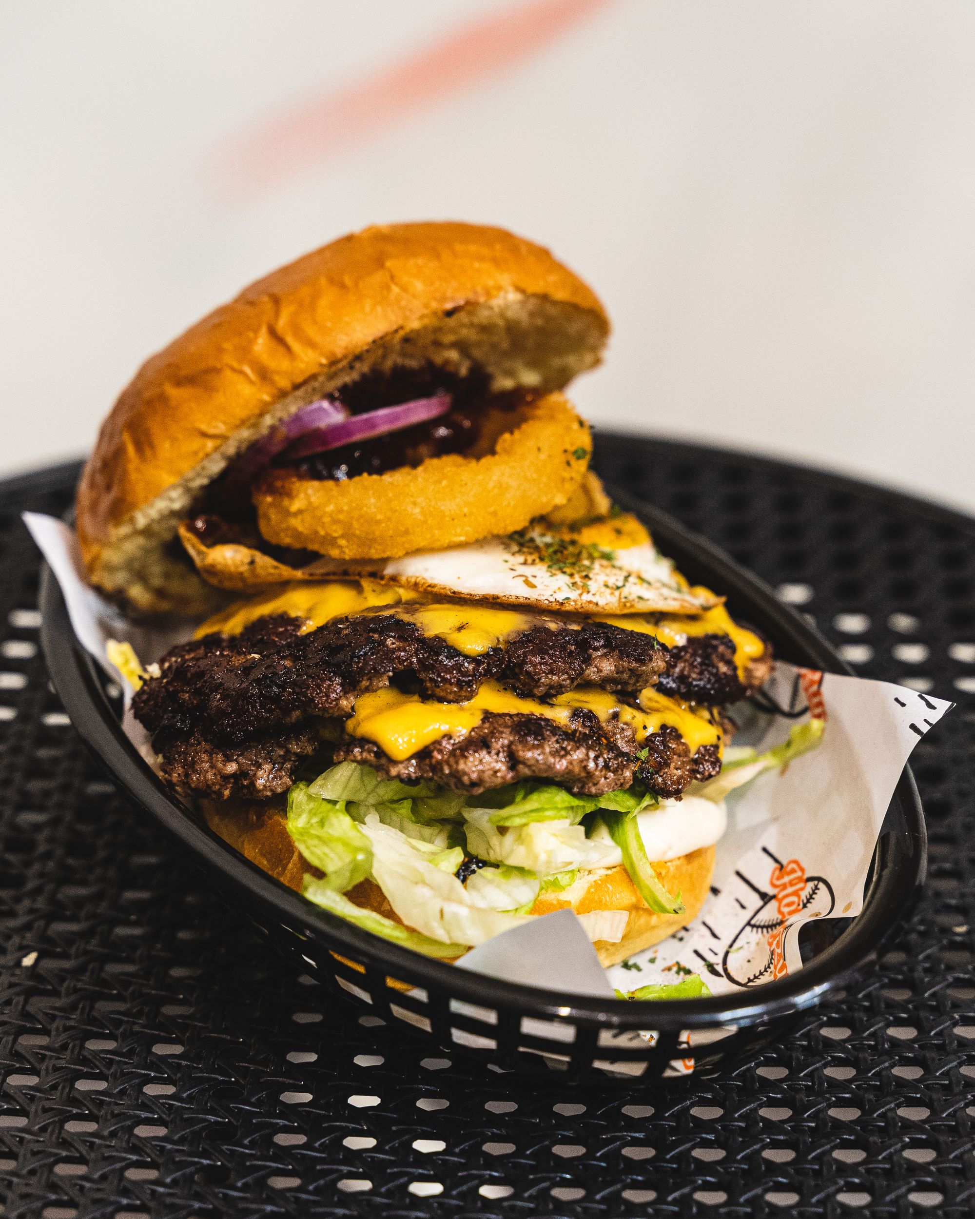 Close up of large burger with two beef patties, cheese, onion ring, egg, onion and lettuce showing