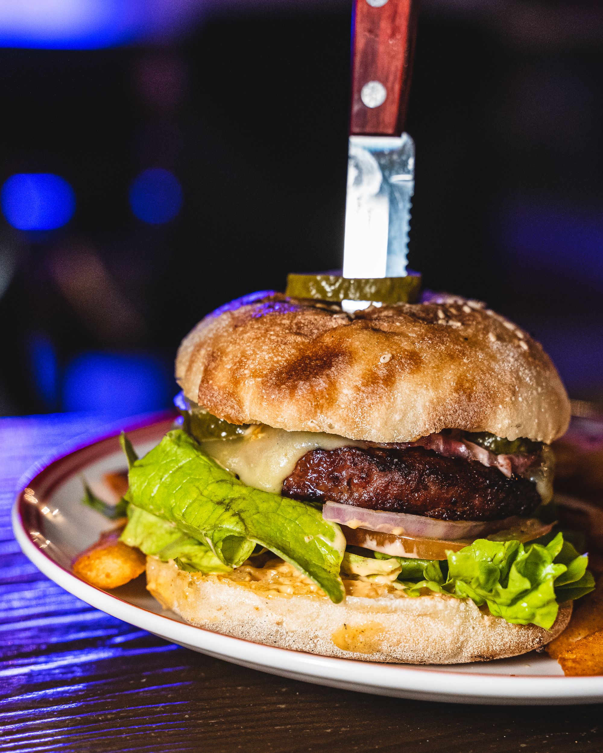 Close up of a beef burger with a knife stuck into it