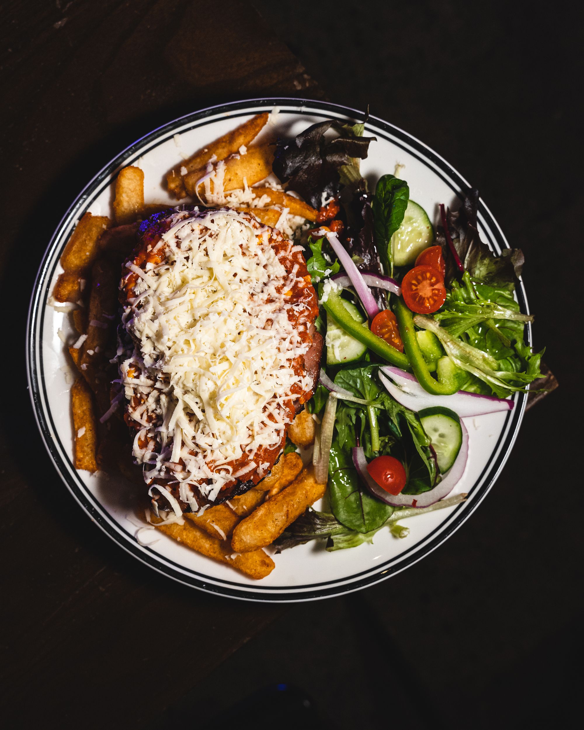 Top down shot of beef parmigiana with shaved cheese, sitting on a bed of chips with a side of salad