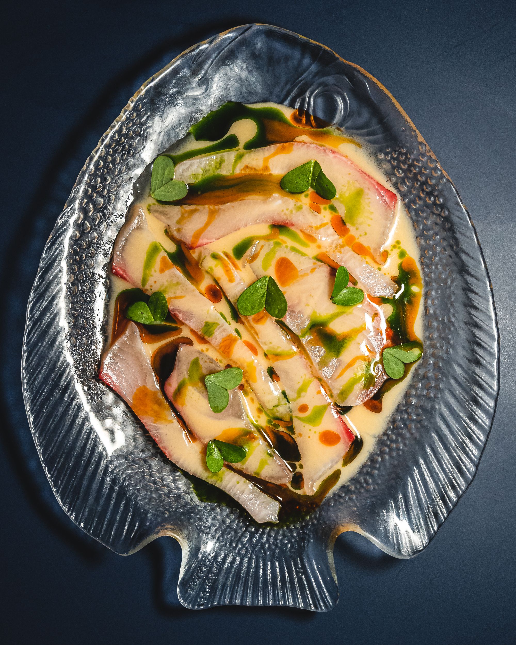 Close up of kingfish ceviche with microherbs on a fish shaped plate