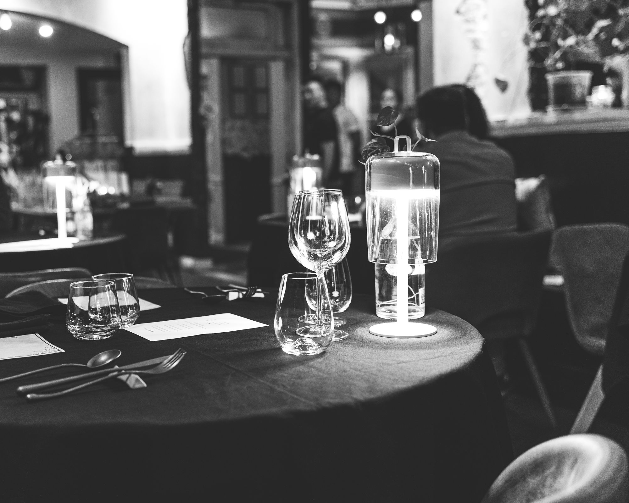 Black and white photo showing glassware and cutlery on a table with a black tablecloth