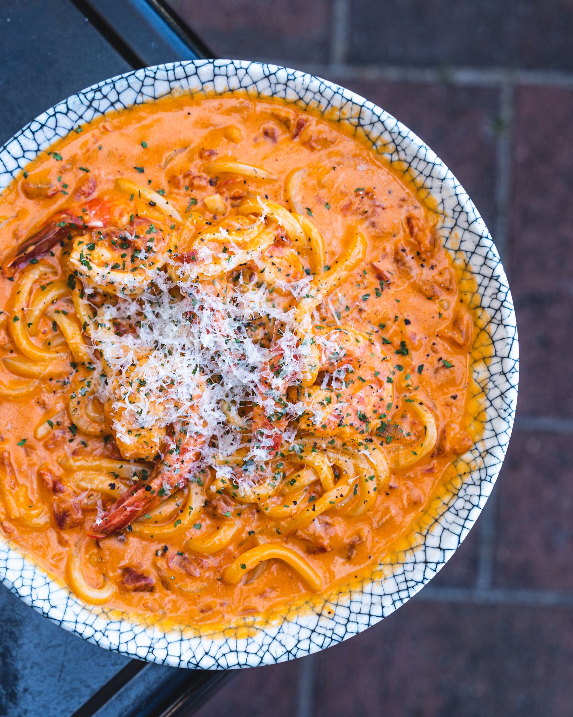 Top down of creamy tomato udon with shaved cheese and prawn on top