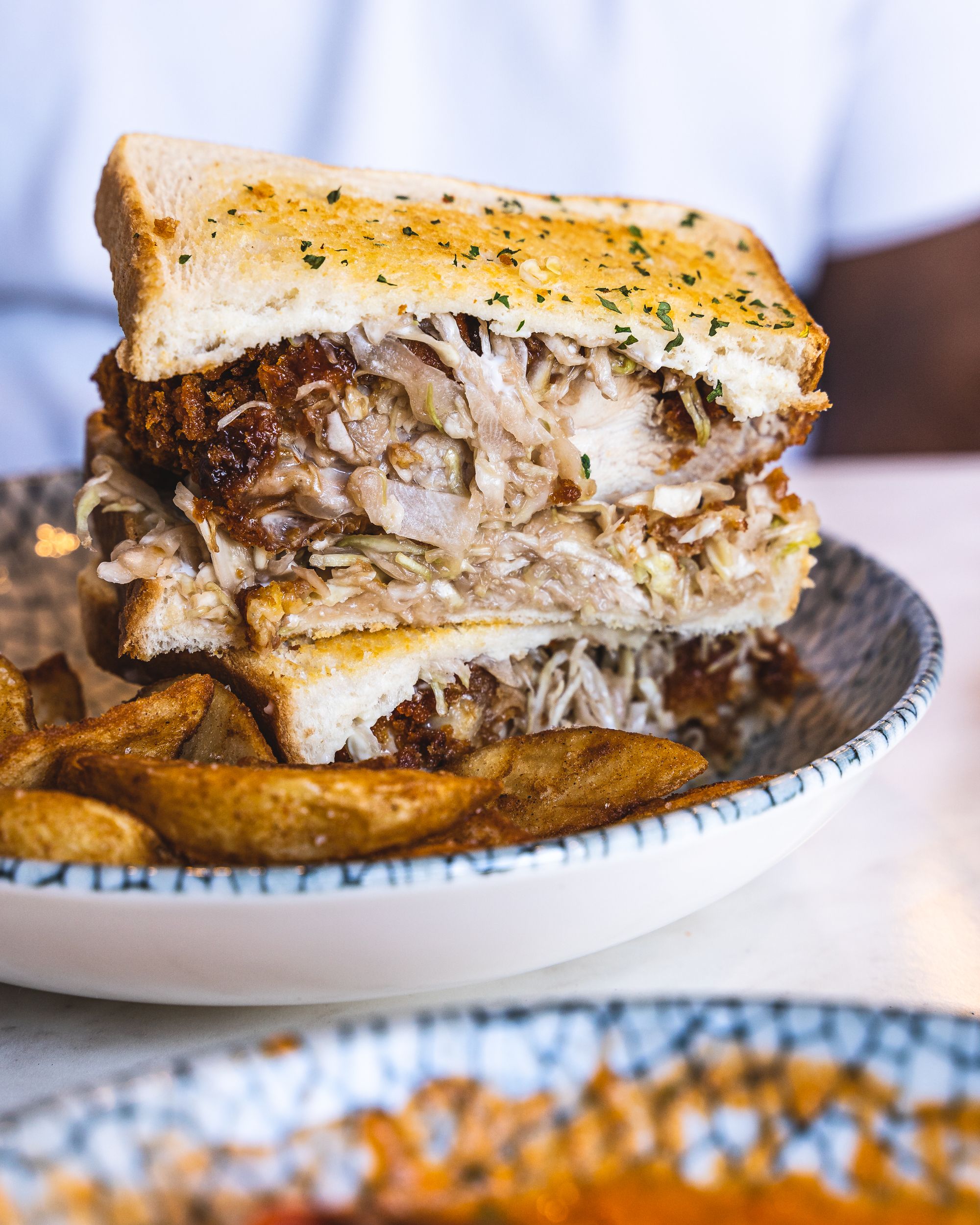 Close up of chicken katsu sando with potato wedges in the foreground