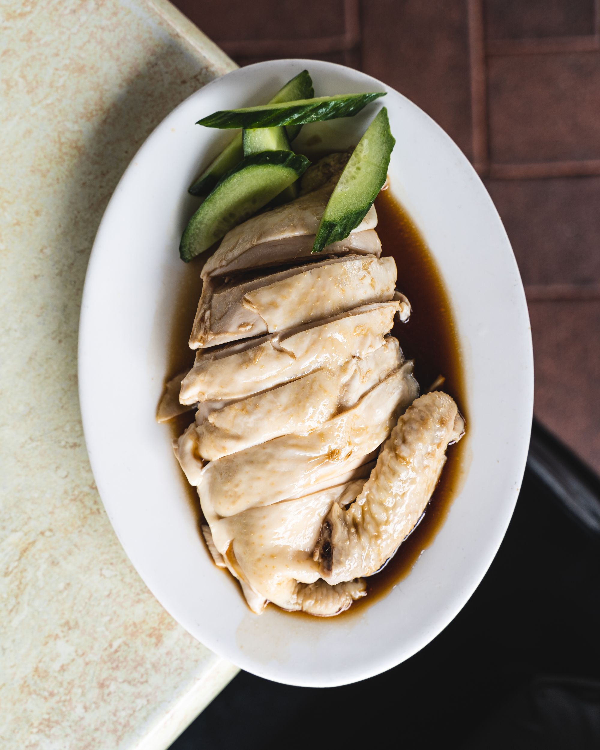 Top down shot of chicken cut into pieces with soy sauce and cucumber