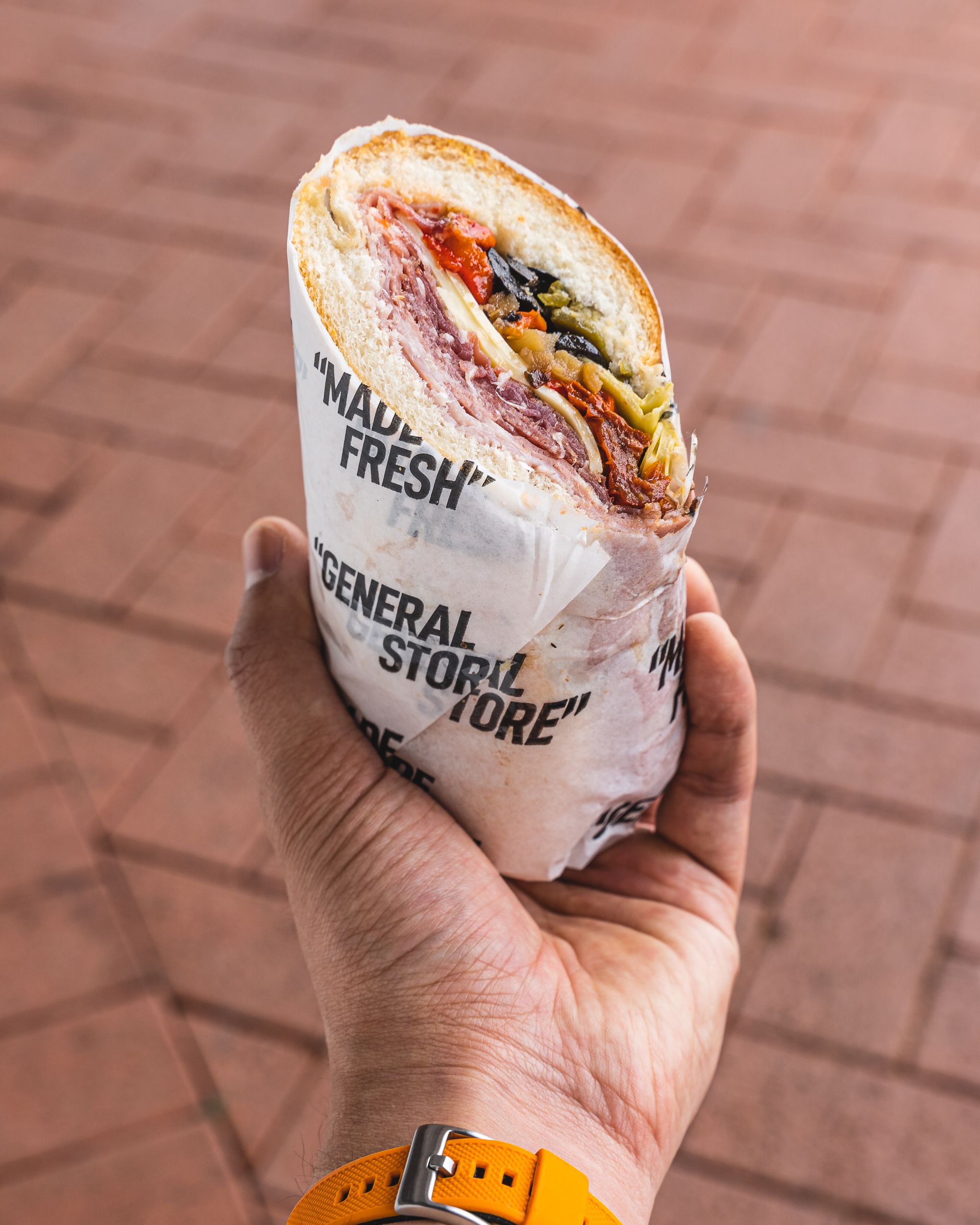 Hand holding a Italian style sandwich wrapped in paper that says "General Store"