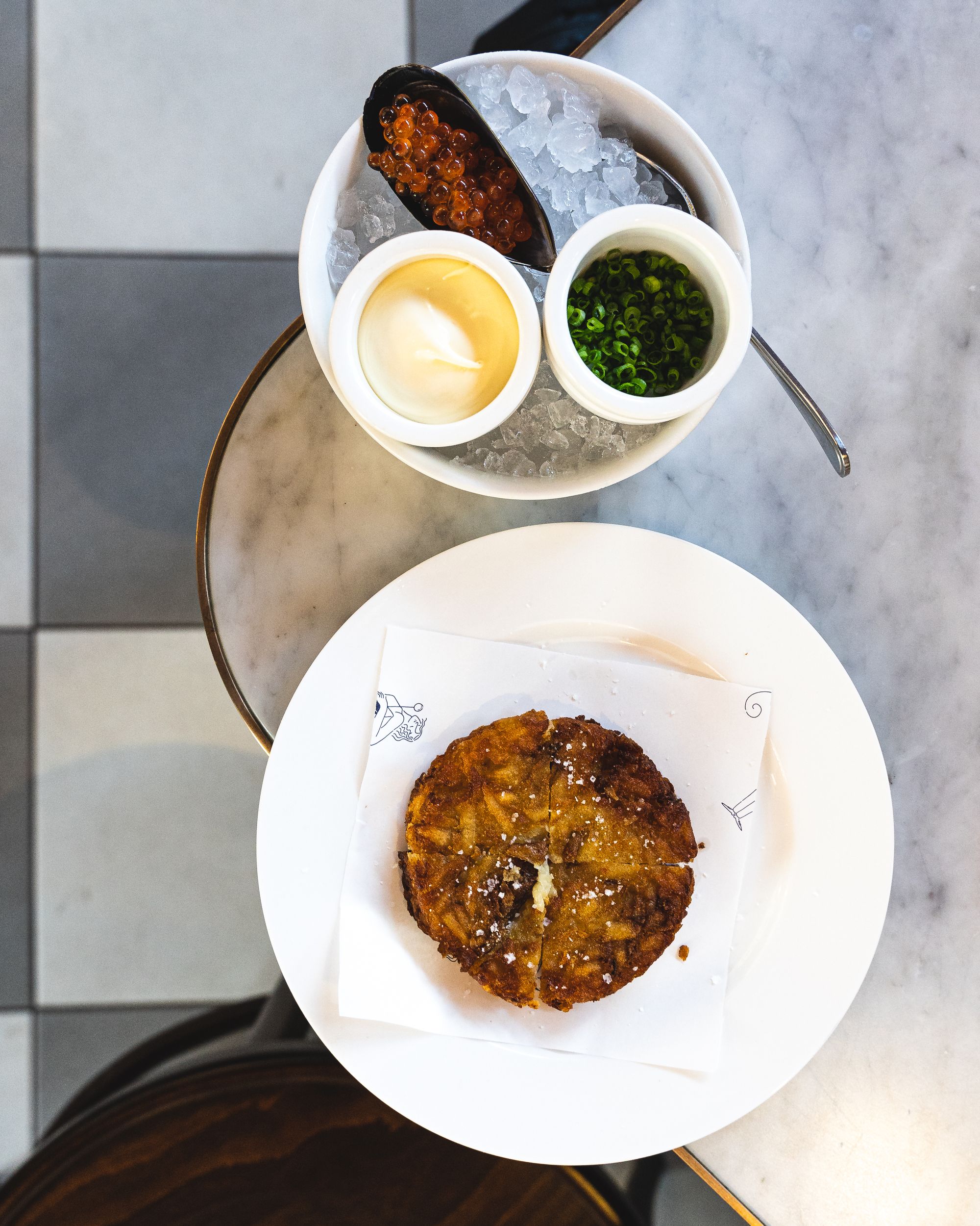 Top down shot of potato rosti on one plate and condiments (mayo, chives and salmon roe) on the other