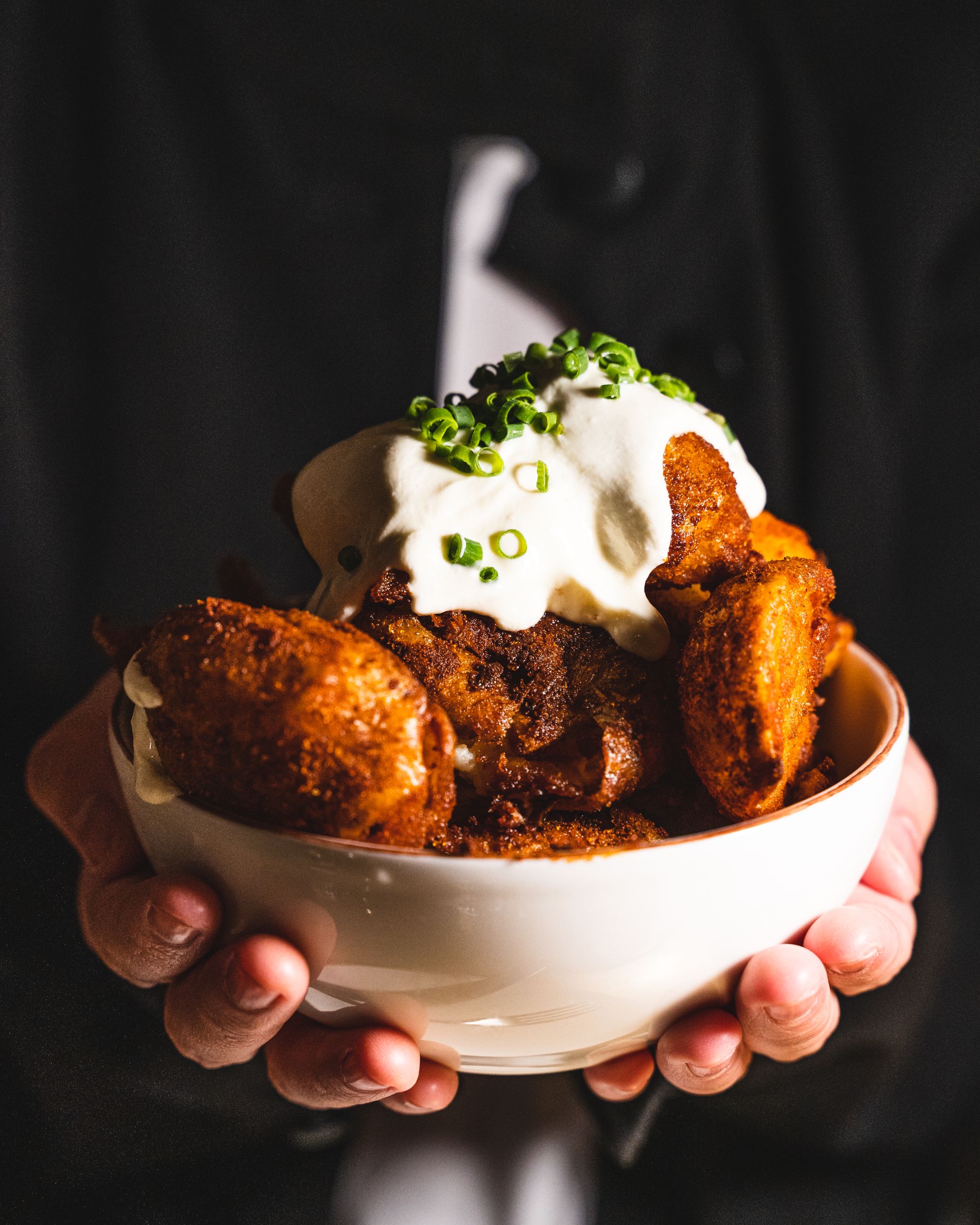 Hand holding a bowl of potatoes with sour cream