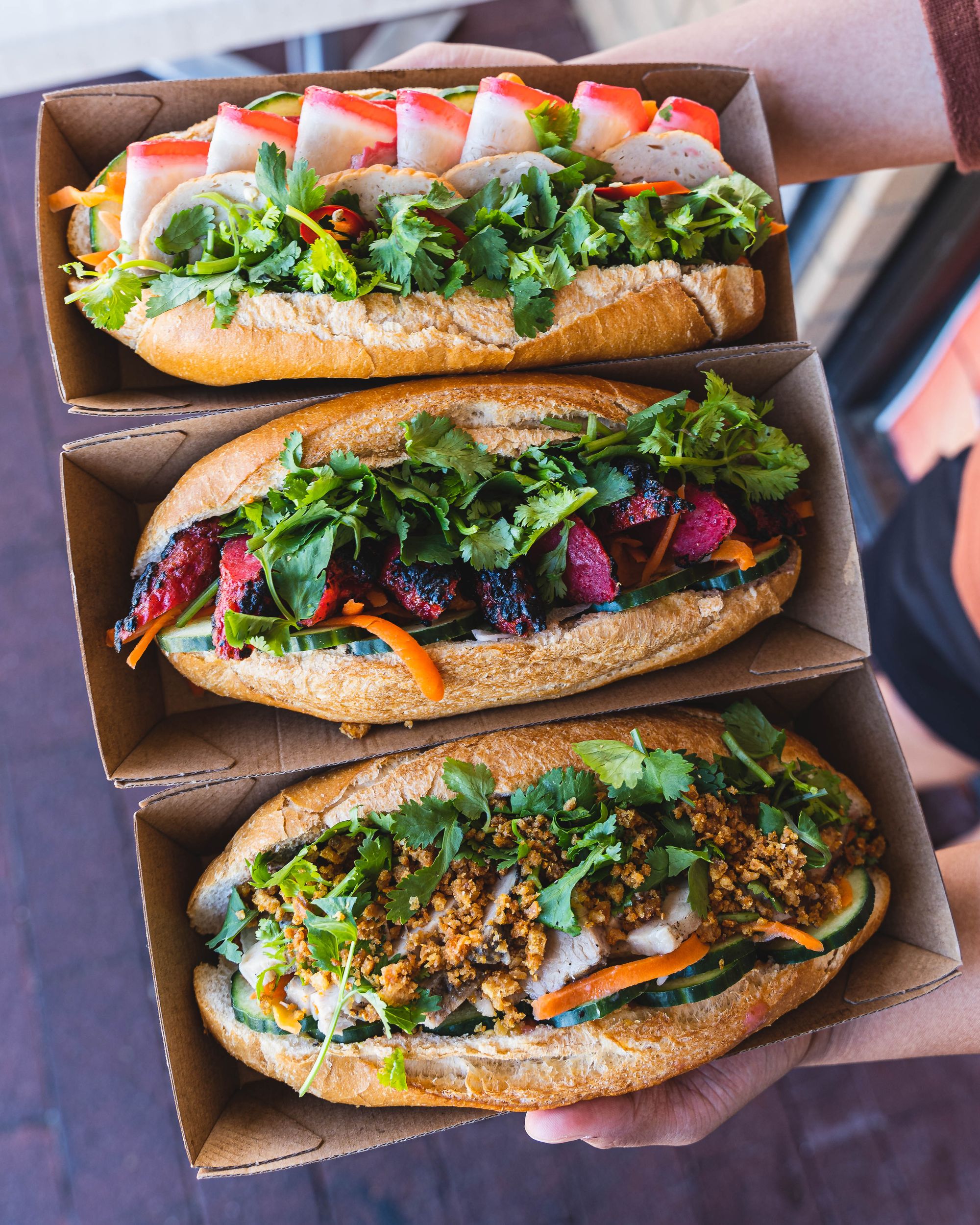 Hand holding three trays each with banh mi