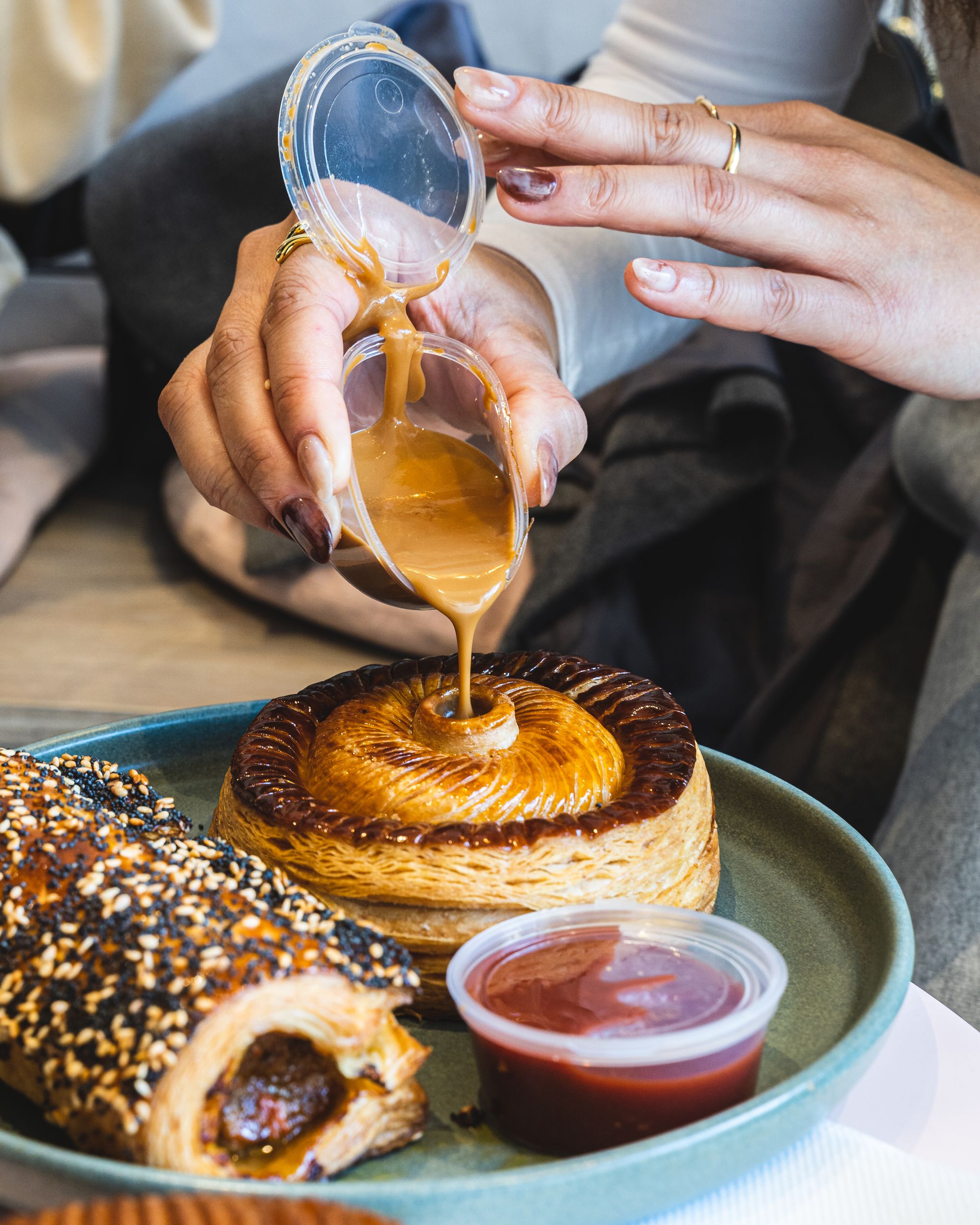 Manicured nails pouring sauce into a pastry