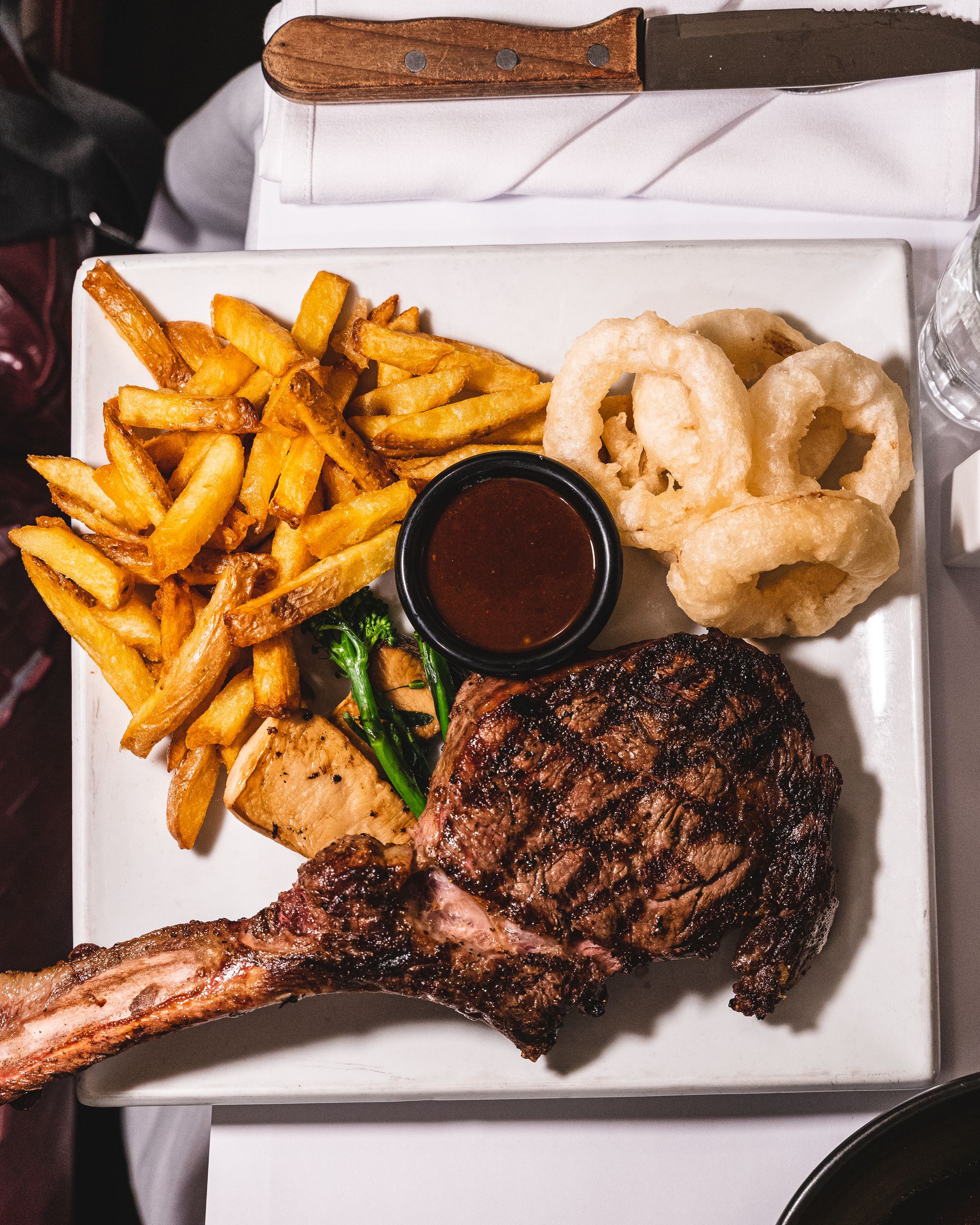 Overhead shot of dry age rib-eye steak with fries, onion rings, mushrooms and greens