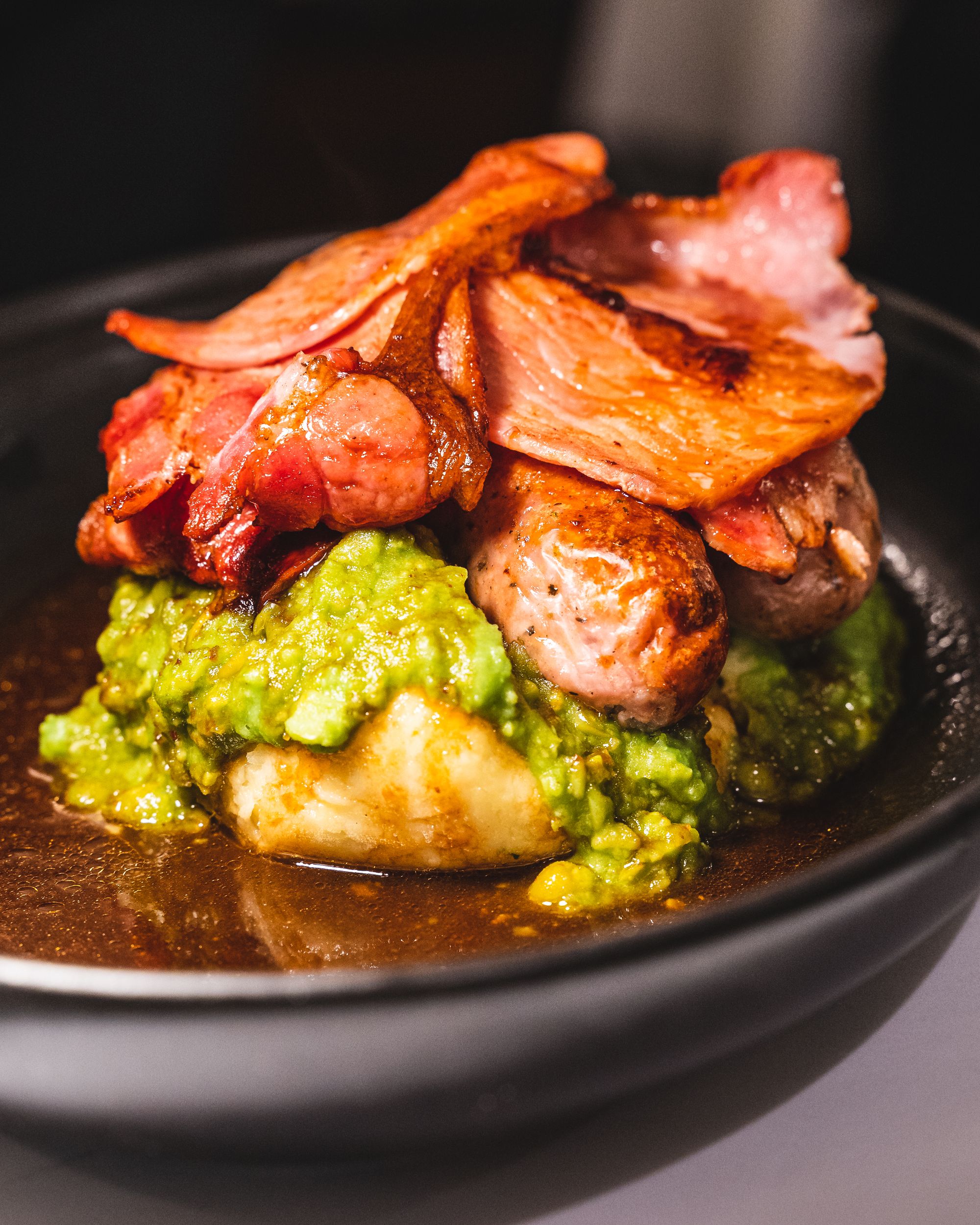 Close up of sausages, mash, peas and bacon