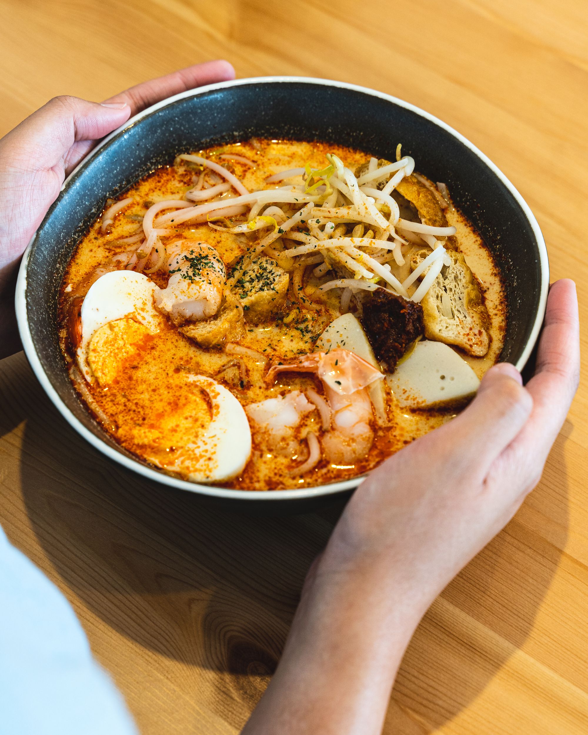 Hand holding a bowl of laksa