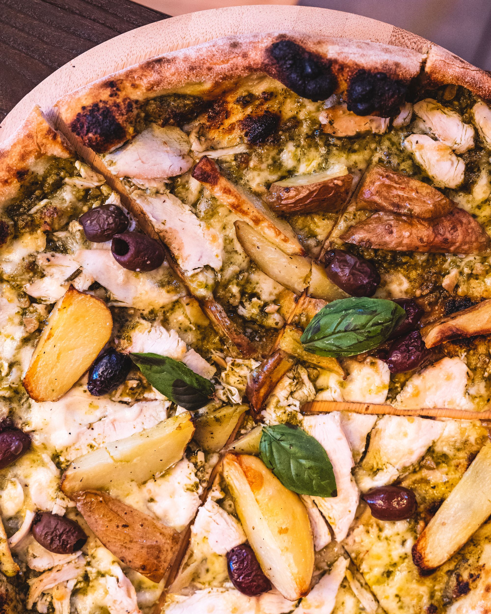 Close up of pizza with basil, olives, potato and cheese