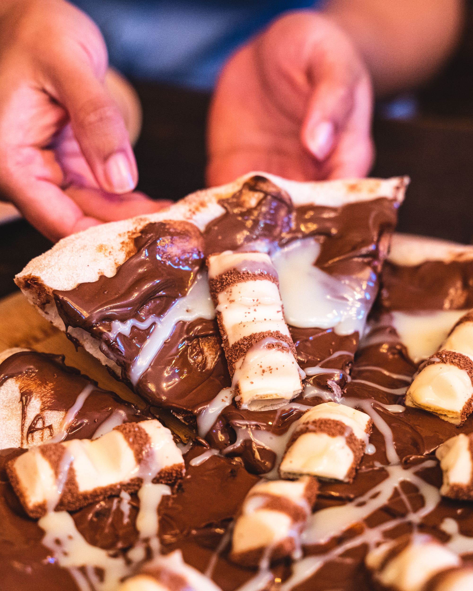 Hand lifting up a slice of pizza with Nutella and Kinder Bueno topping