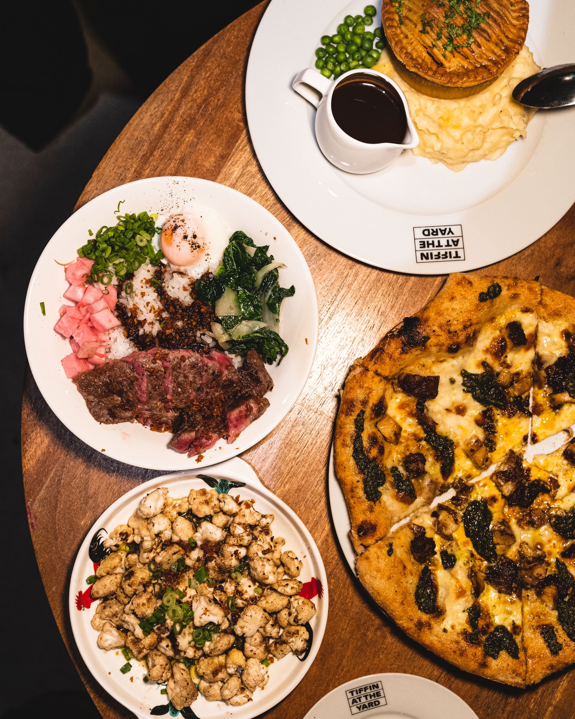 Overhead shot of pie, a steak bowl, roasted cauliflower and pizza