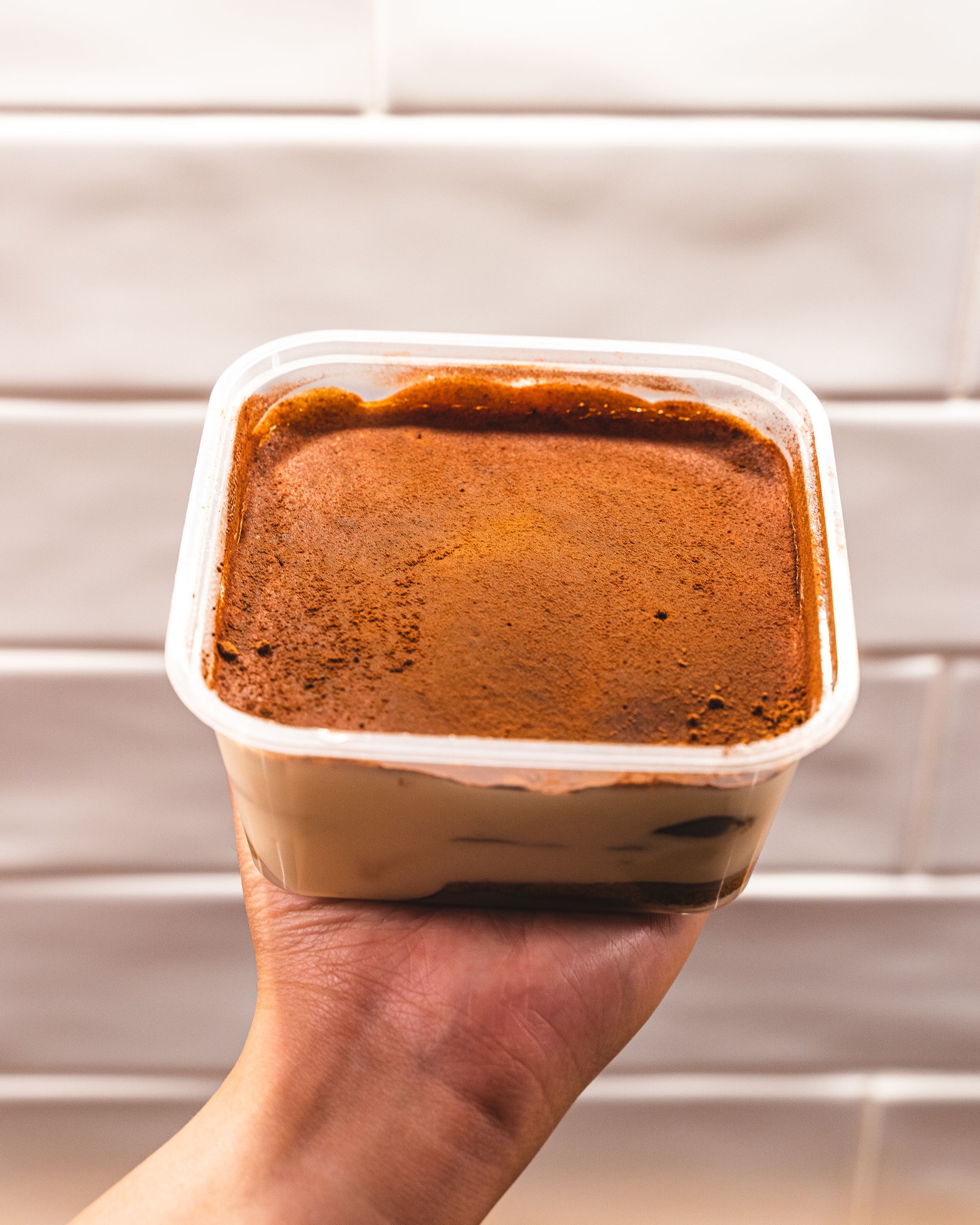 Hand holding tiramisu in a tub