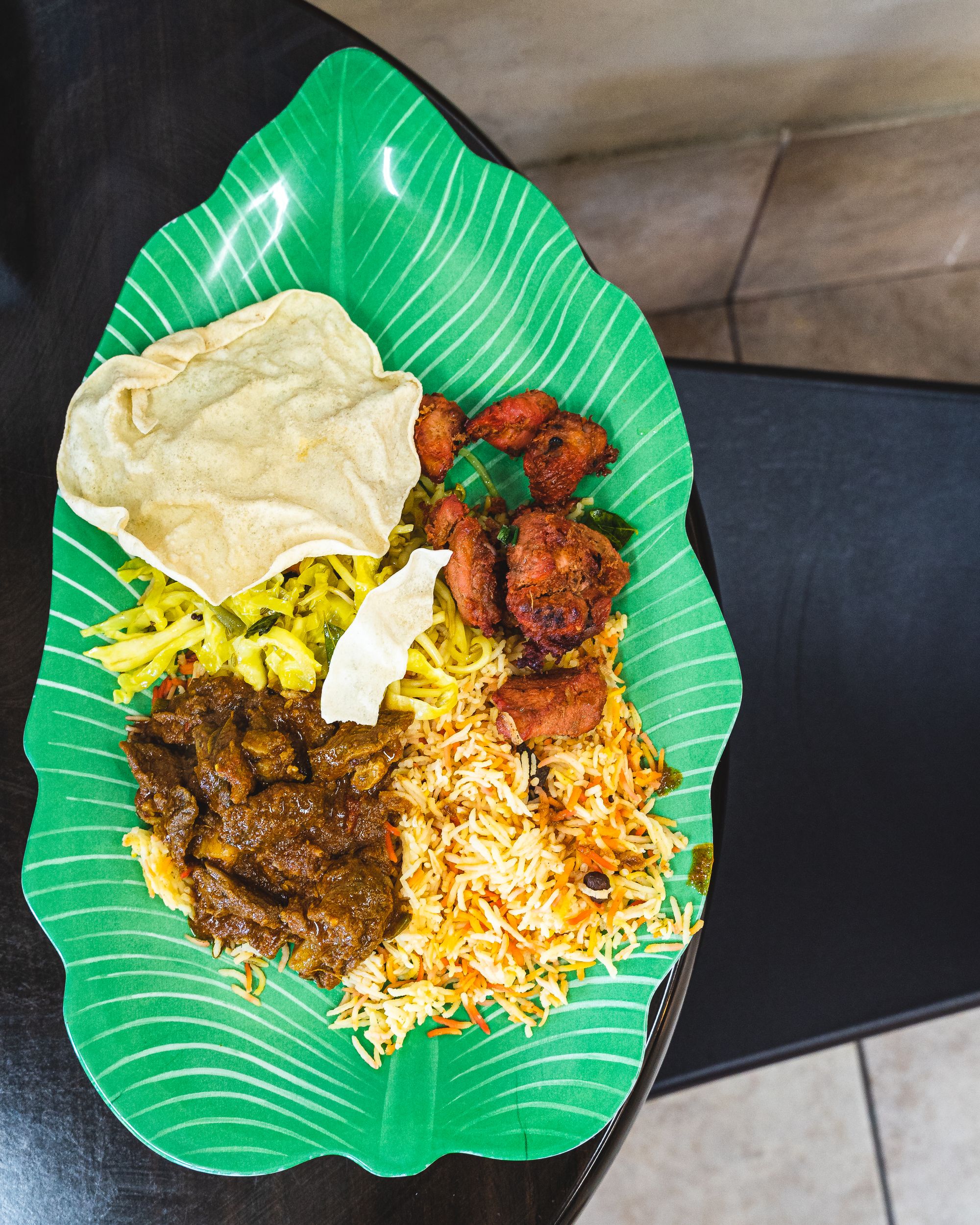 Overhead shot of lamb curry, chicken 65, briyani and pappadum on a leaf shaped plate