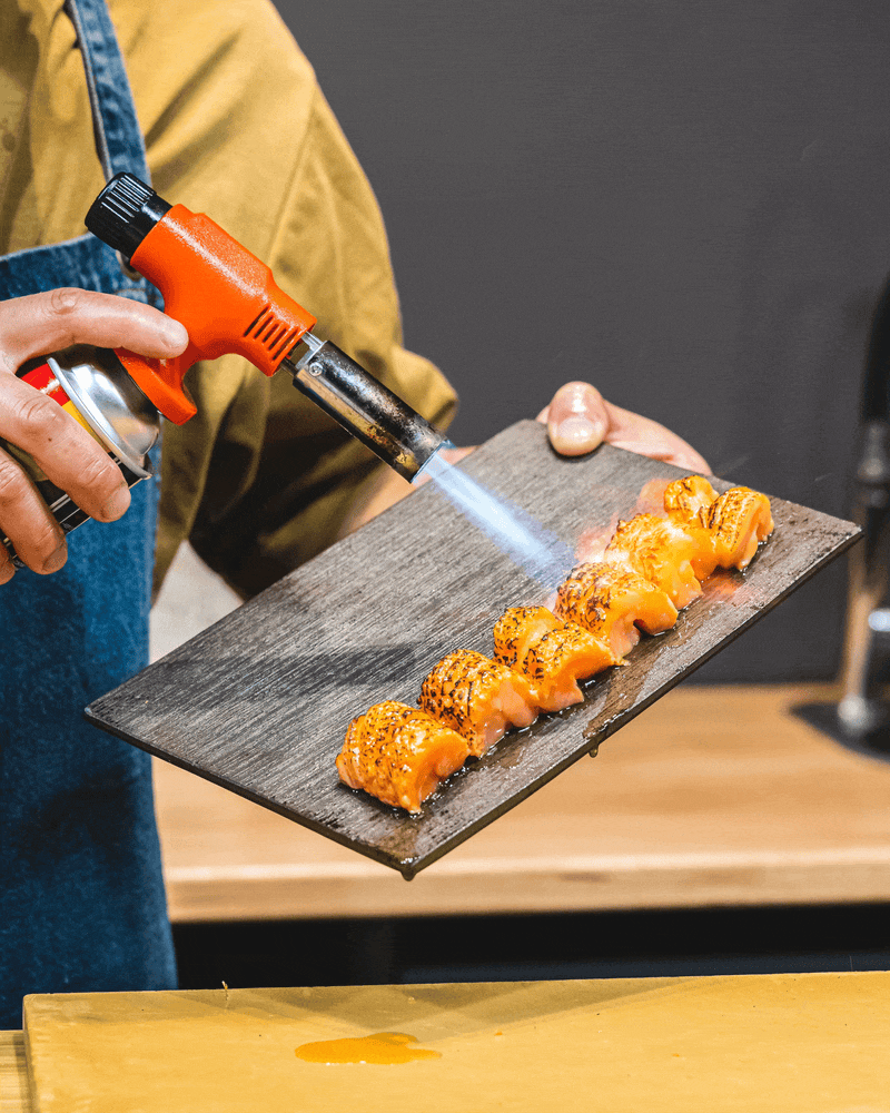 Chef blowtorch searing salmon with oil dripping off