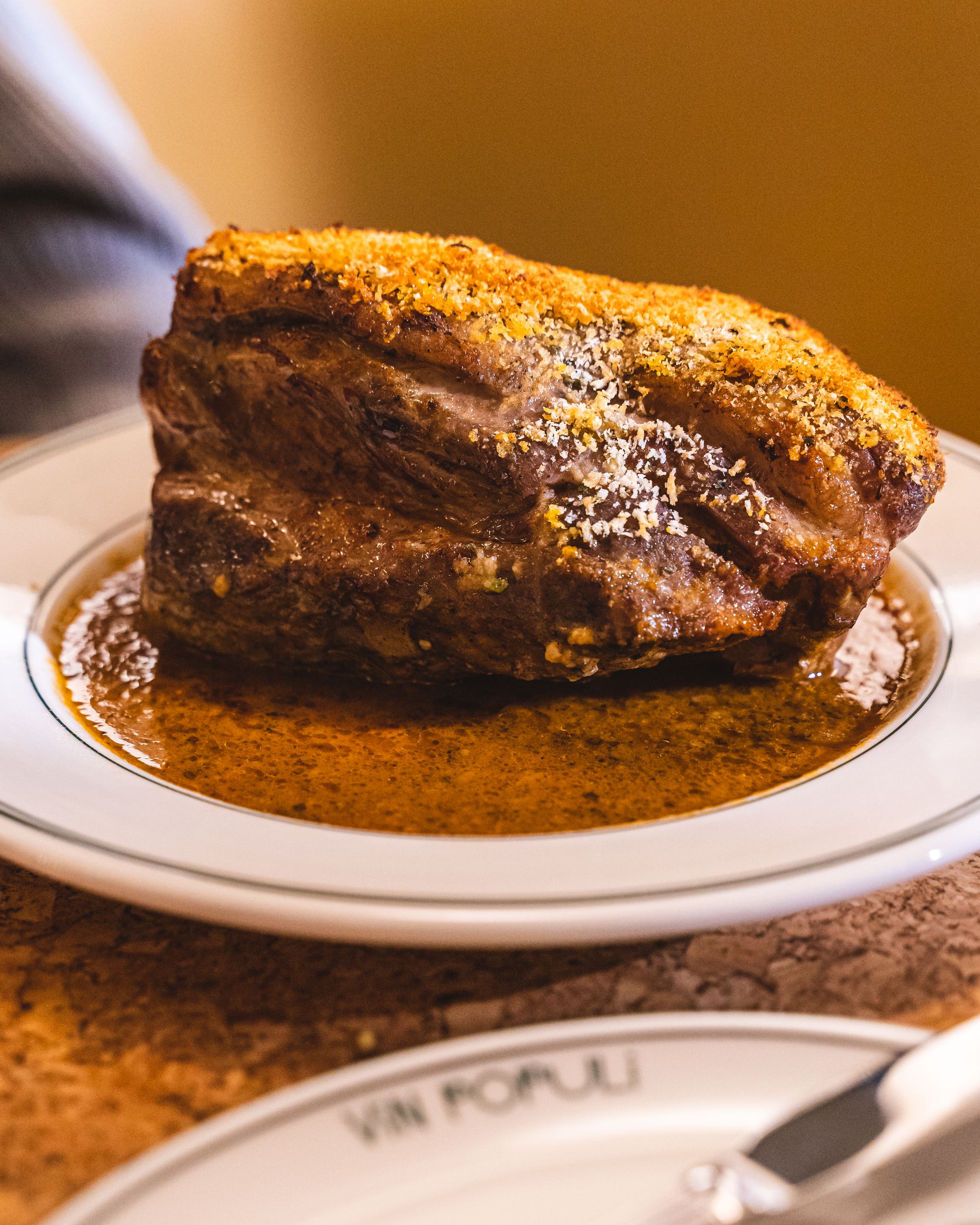 Close up of roast lamb on a plate with "Vin Populi" showing on a different plate in the foreground