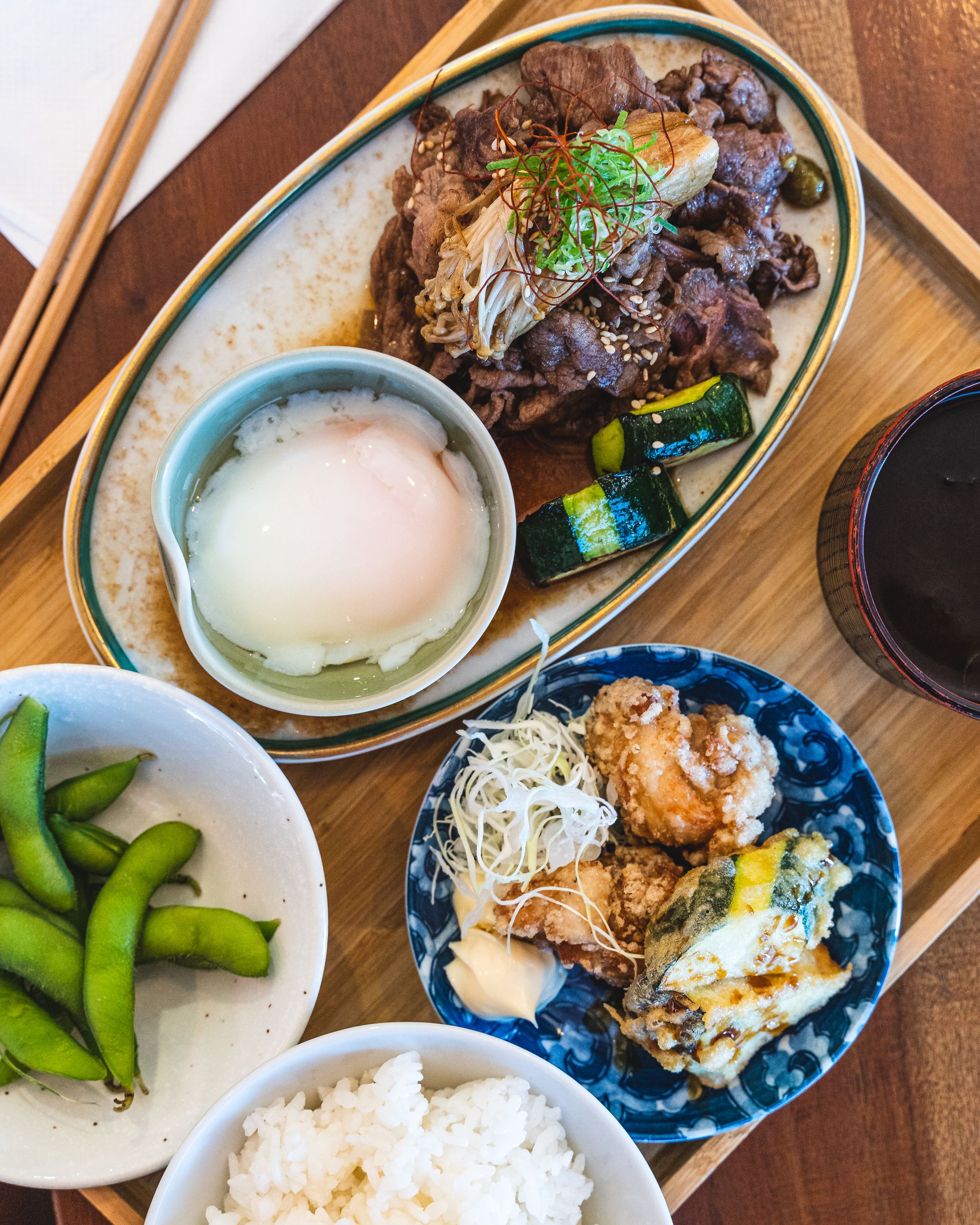 Top down shot of teishoku - edamame, rice, tempura, karaage and cooked slice beef