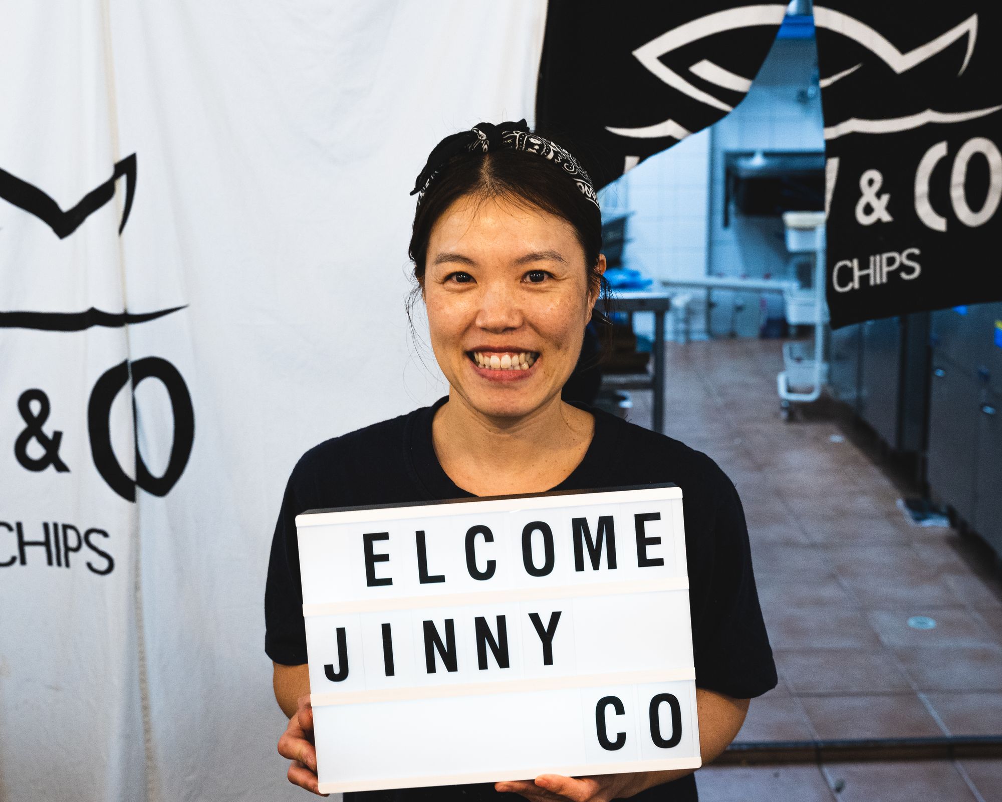 Asian lady holding a sign saying "elcome Jinny Co"
