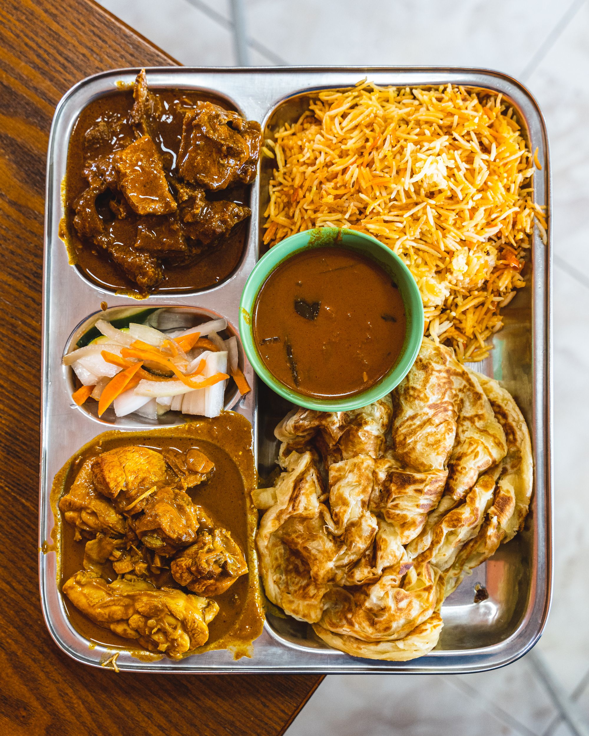 Top down of curry on a silver tray with roti and briyani