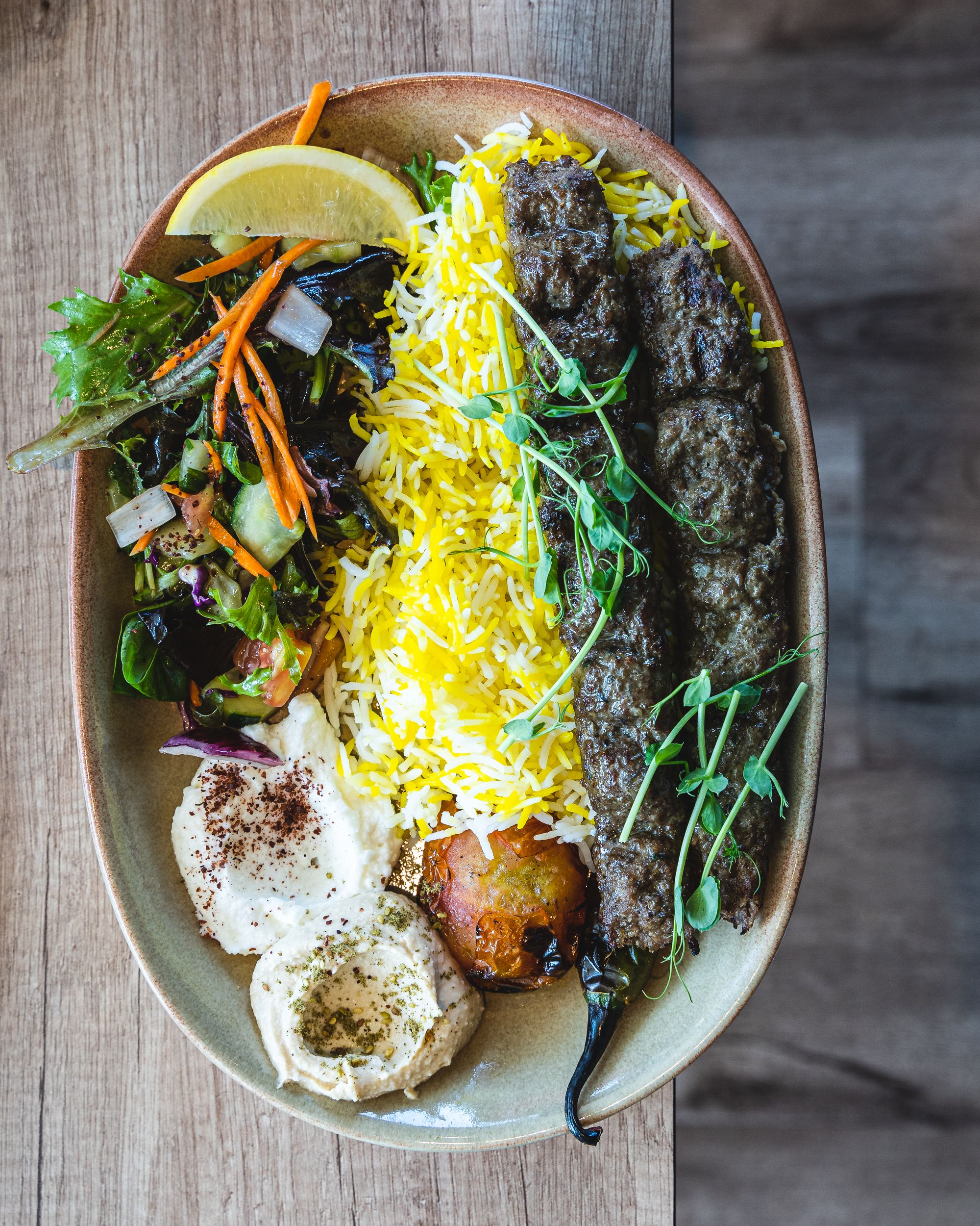 Top down shot of saffron rice, salad, hummuss and two lamb skewers