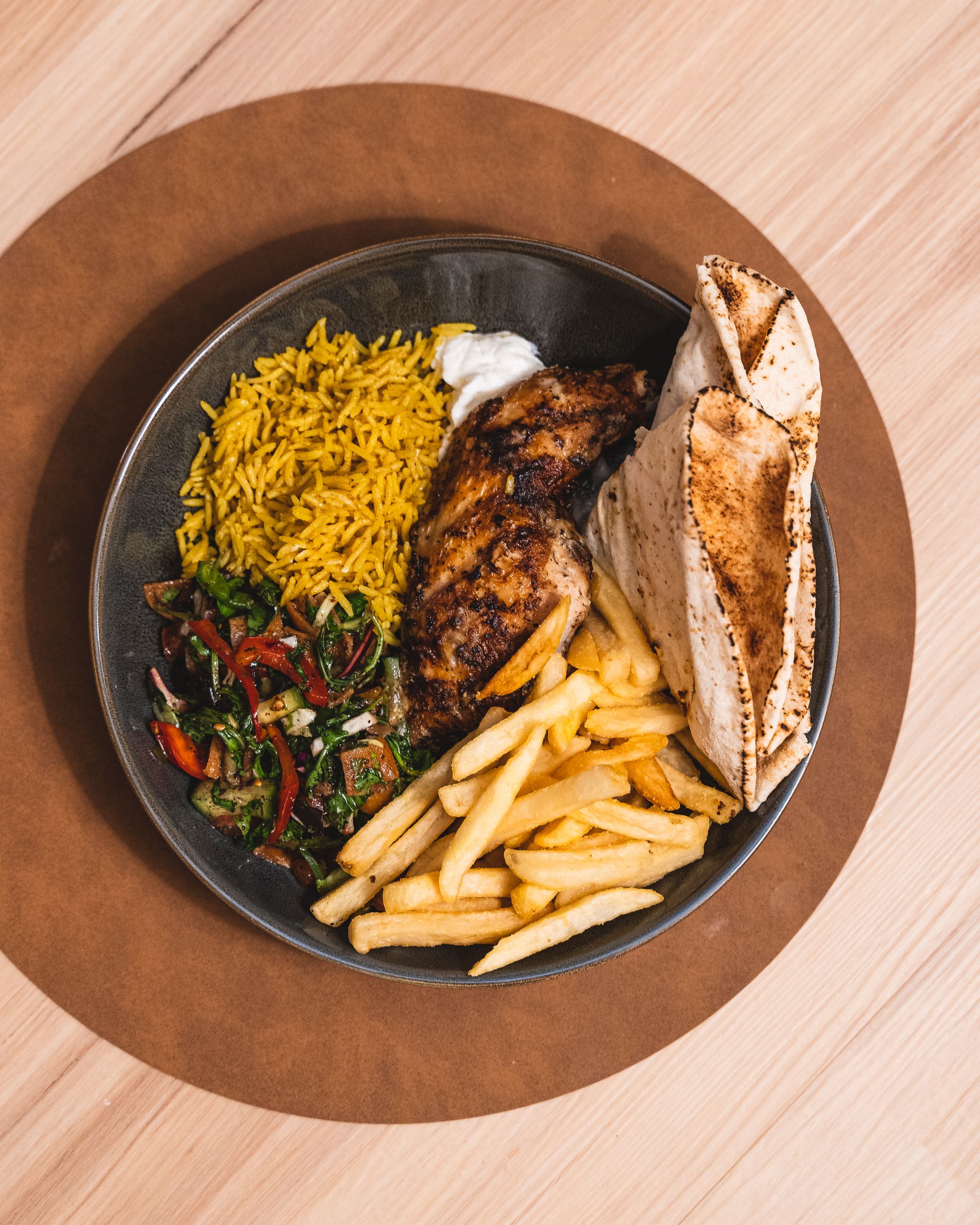 Top down shot of chicken, pita bread, rice, salad and chips in a round circular bowl