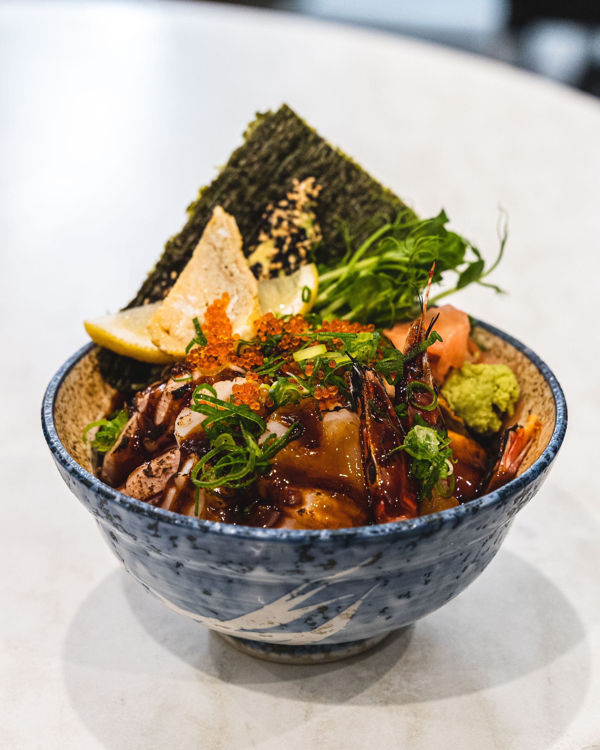 Close up of aburi sashimi in a rice bowl, topped with dark sauce