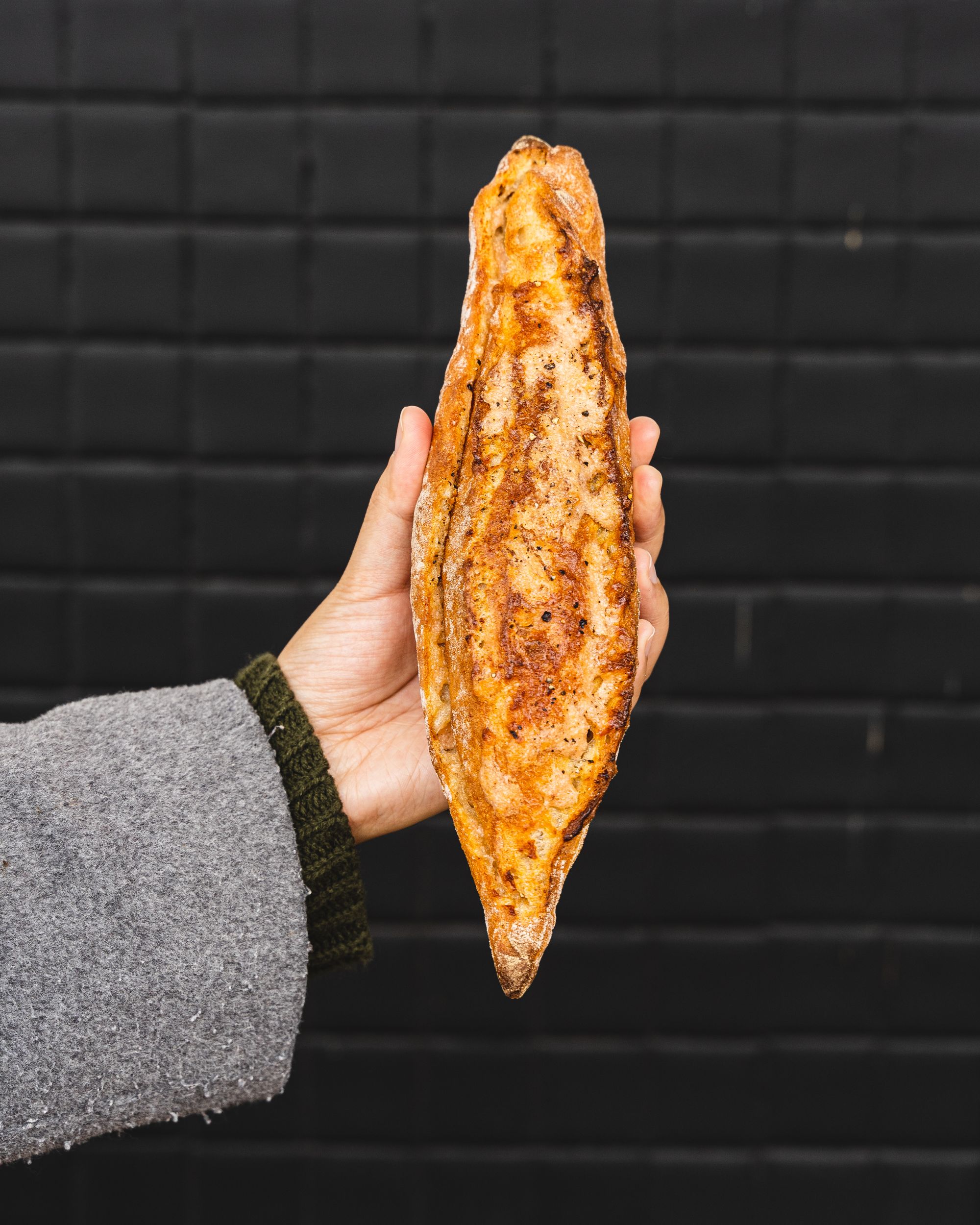 Hand holding a baguette against a black background