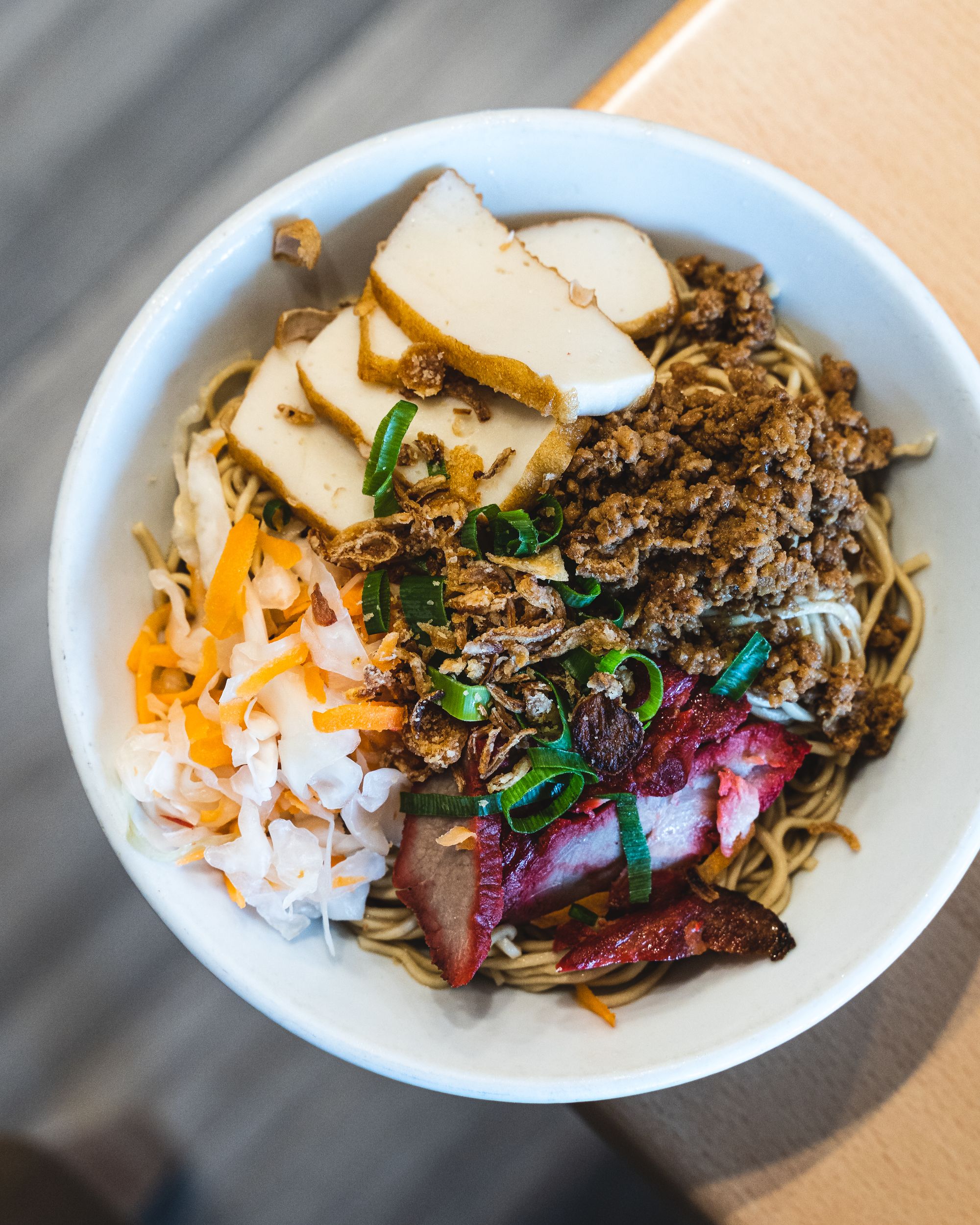 Top down shot of noodles, mince meat, fishcake, pickled cabbage and raddish and BBQ pork