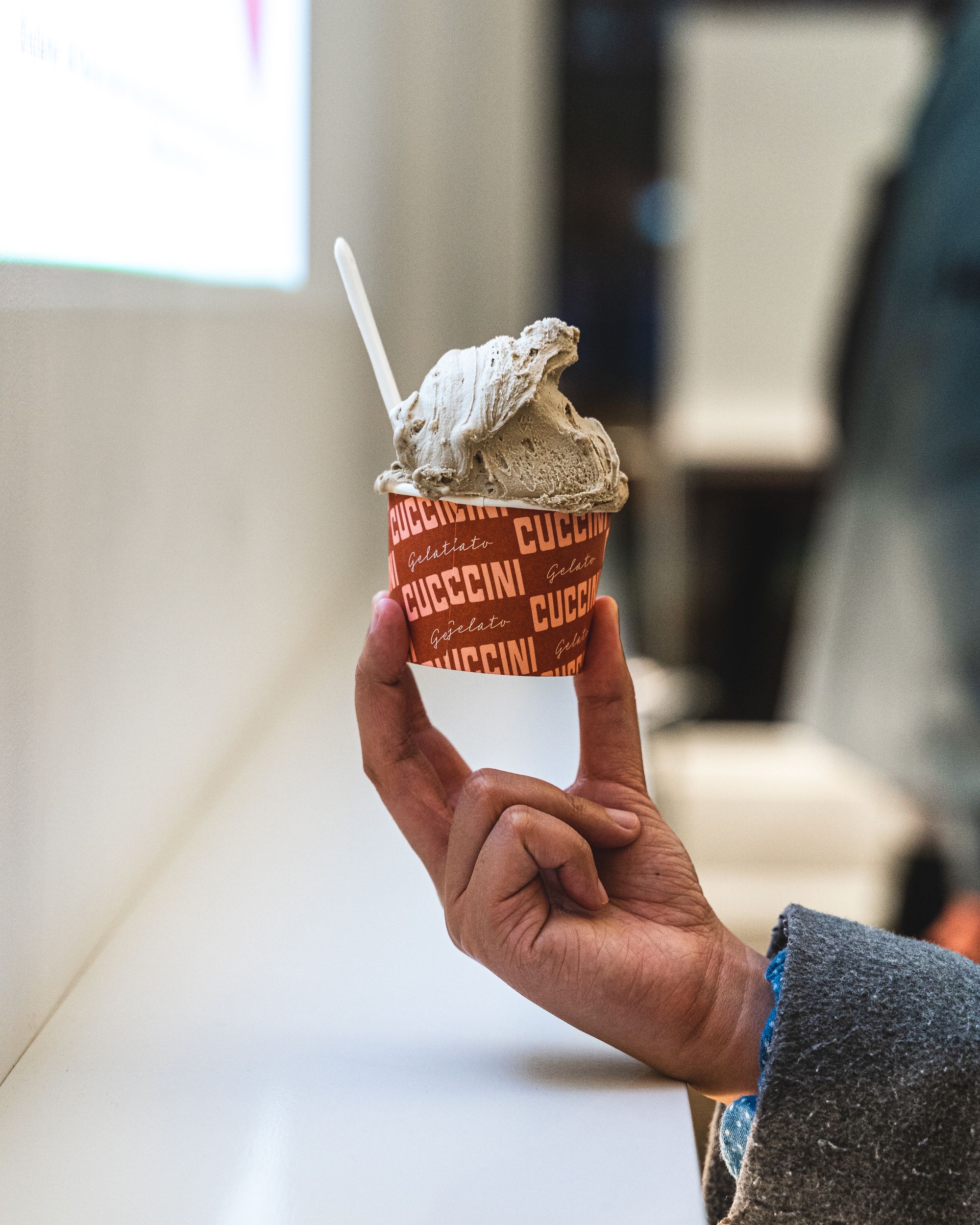 Hand holding gelato in a cup with the words "Cuccini" printed on it