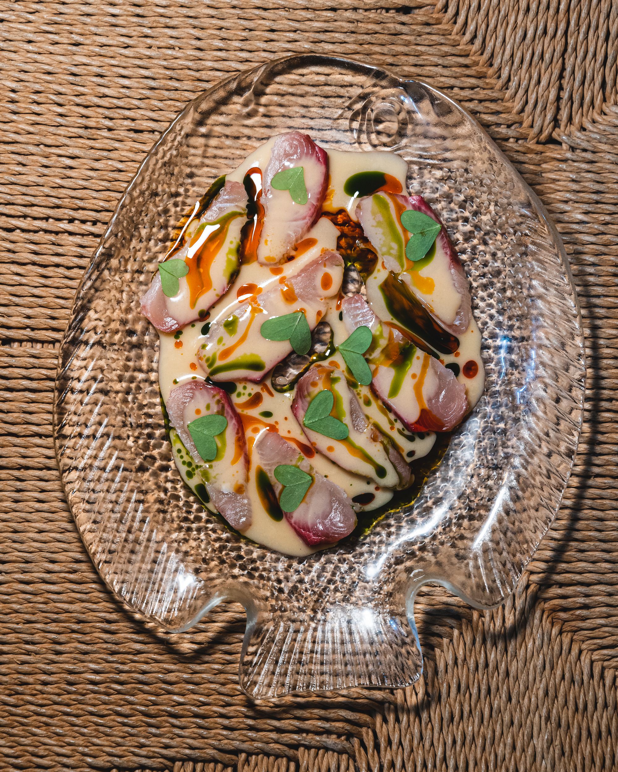 Kingfish ceviche with a creamy coloured sauce and green heart shaped herbs