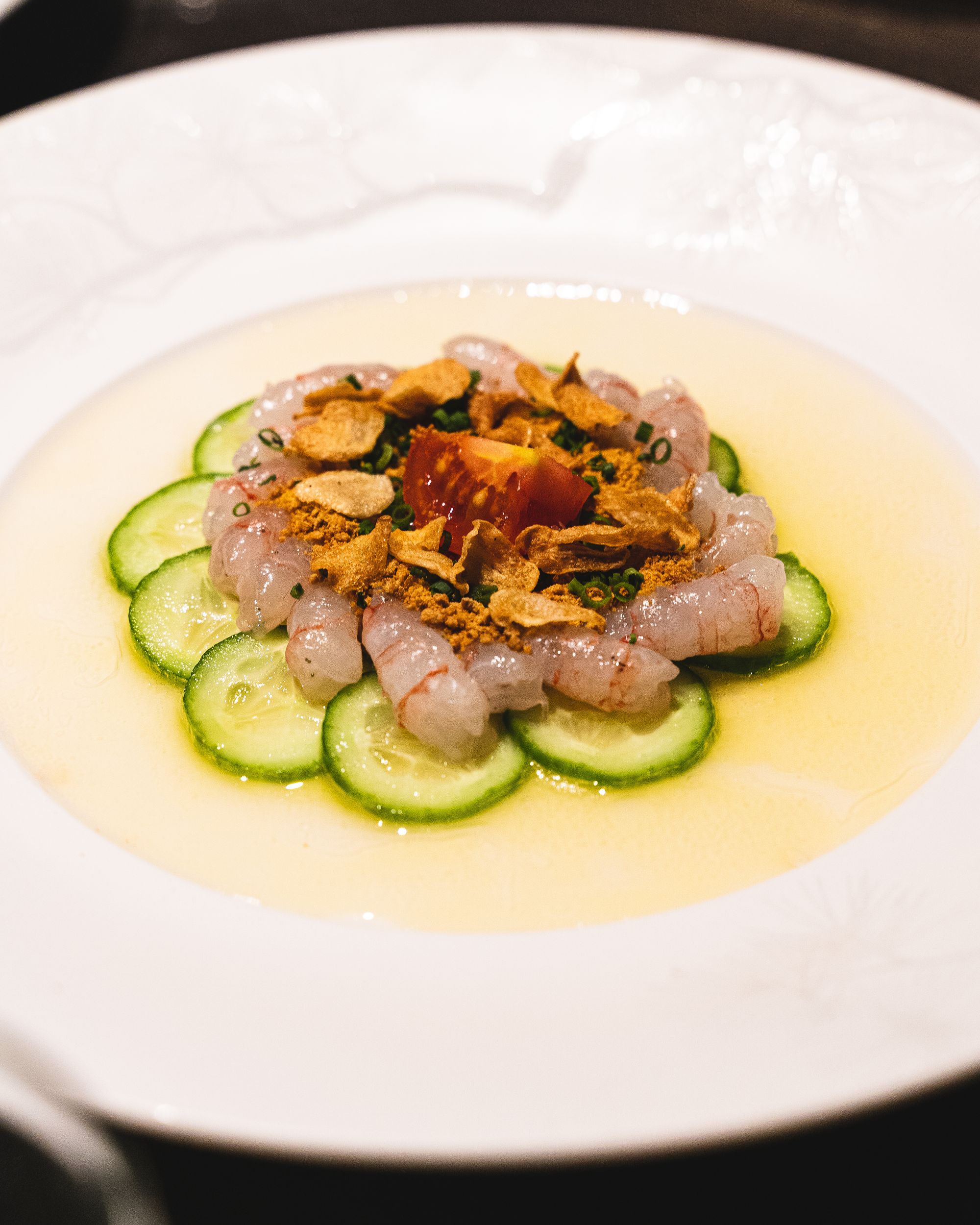 Close up of amaebi sashimi sitting on-top of a bed of cucumber surrounded by a citrus looking sauce