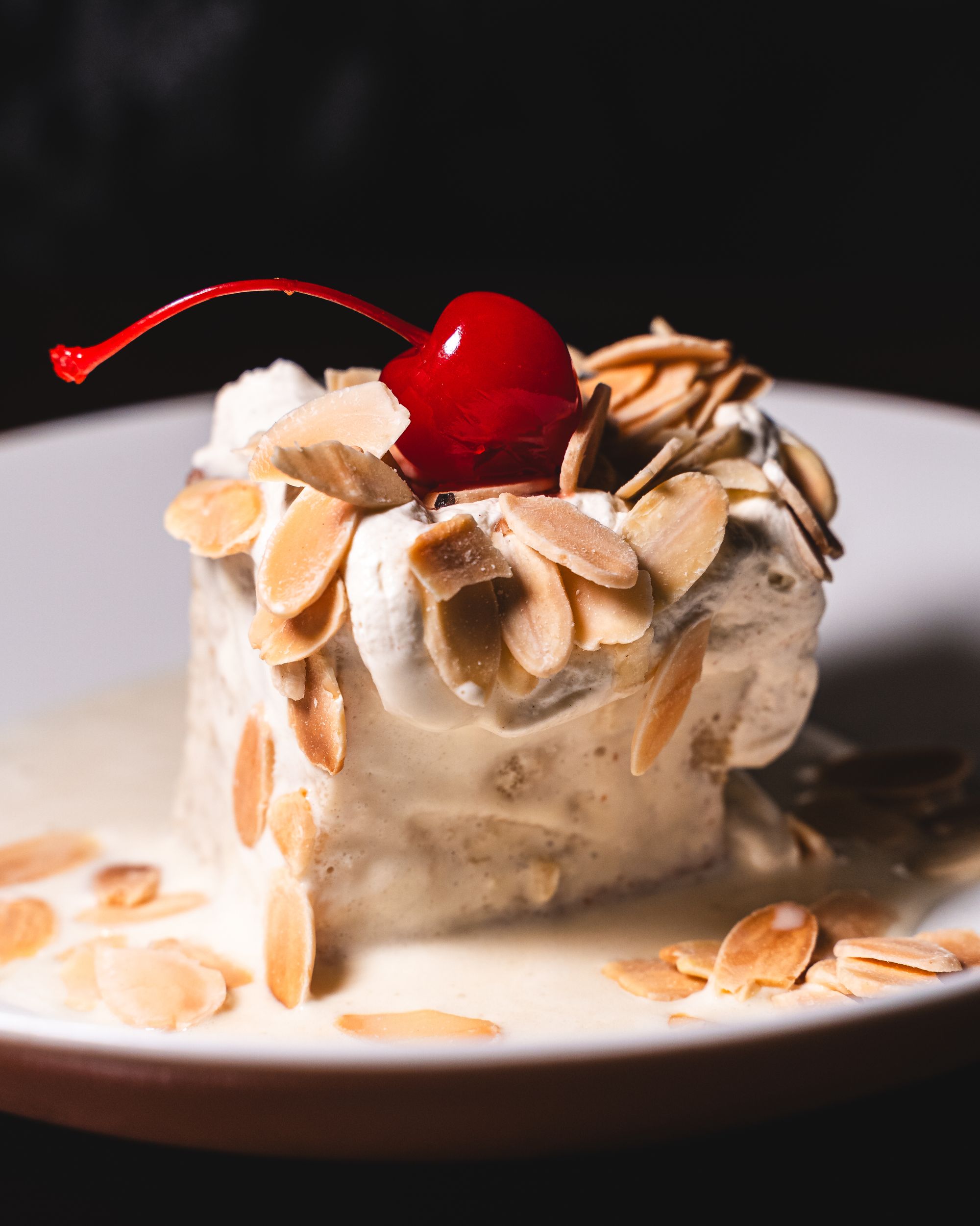 Close up of cake with cream, almonds and a cherry on top