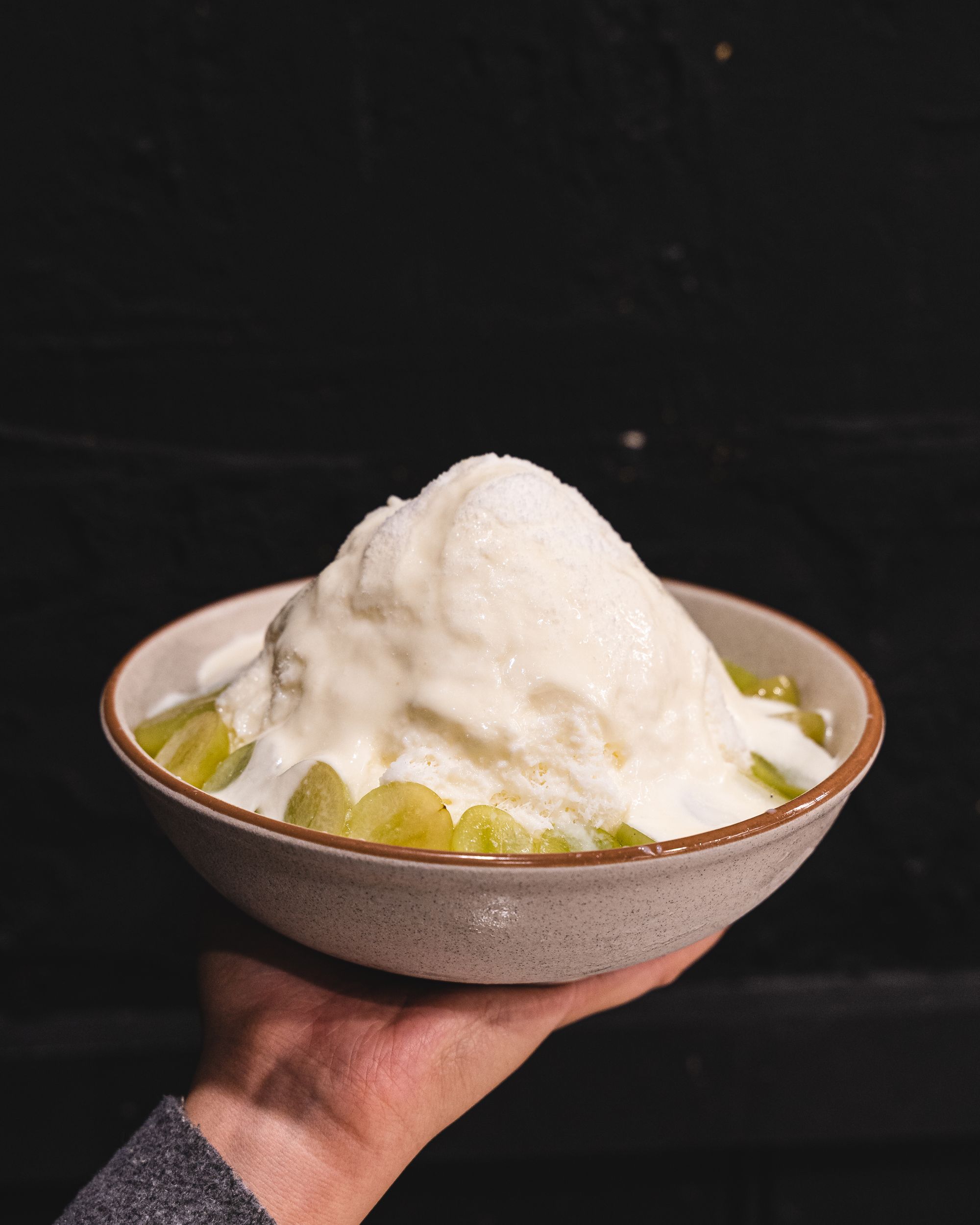 Hand holding a bowl of shaved ice dessert with grape