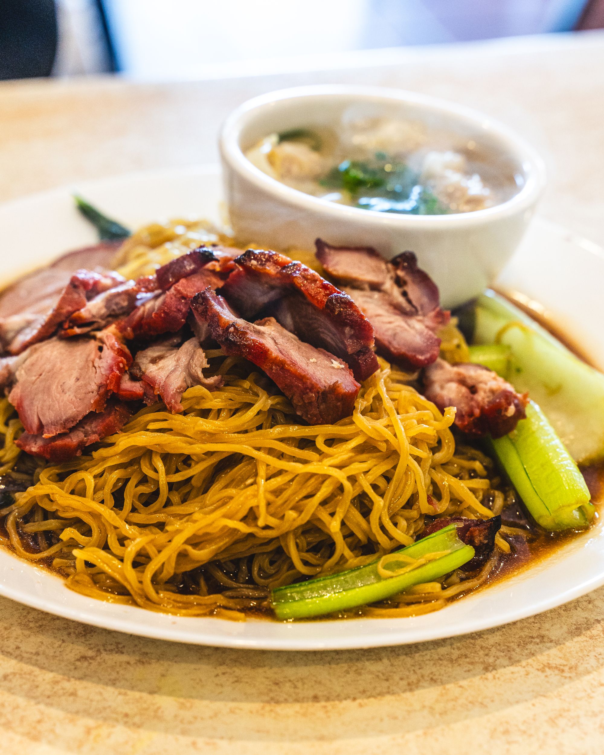 Close up of wonton noodles with BBQ pork and a bowl of wonton in the back