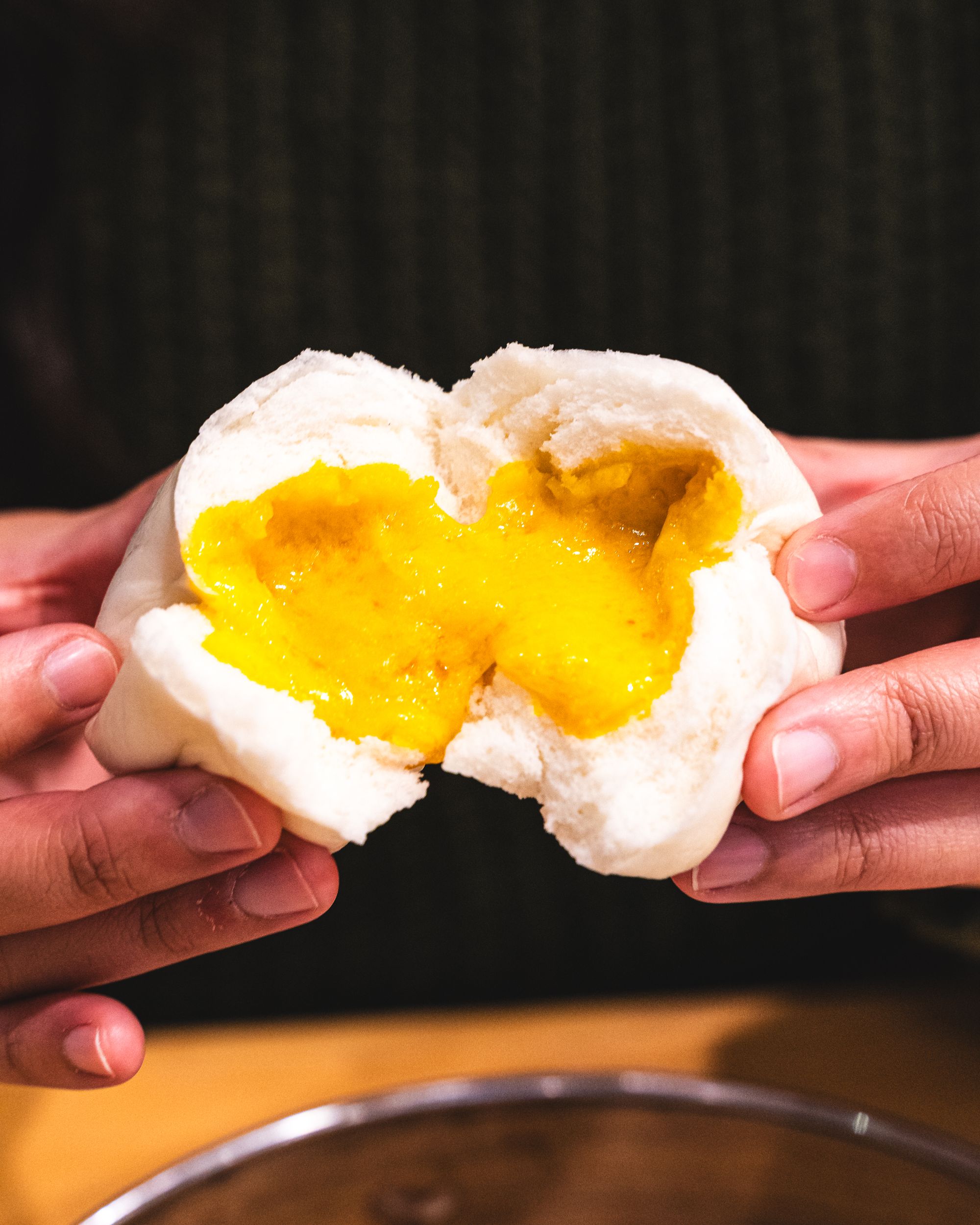 Hand holding a salted egg custard bun split open showing the oozing salted egg custard