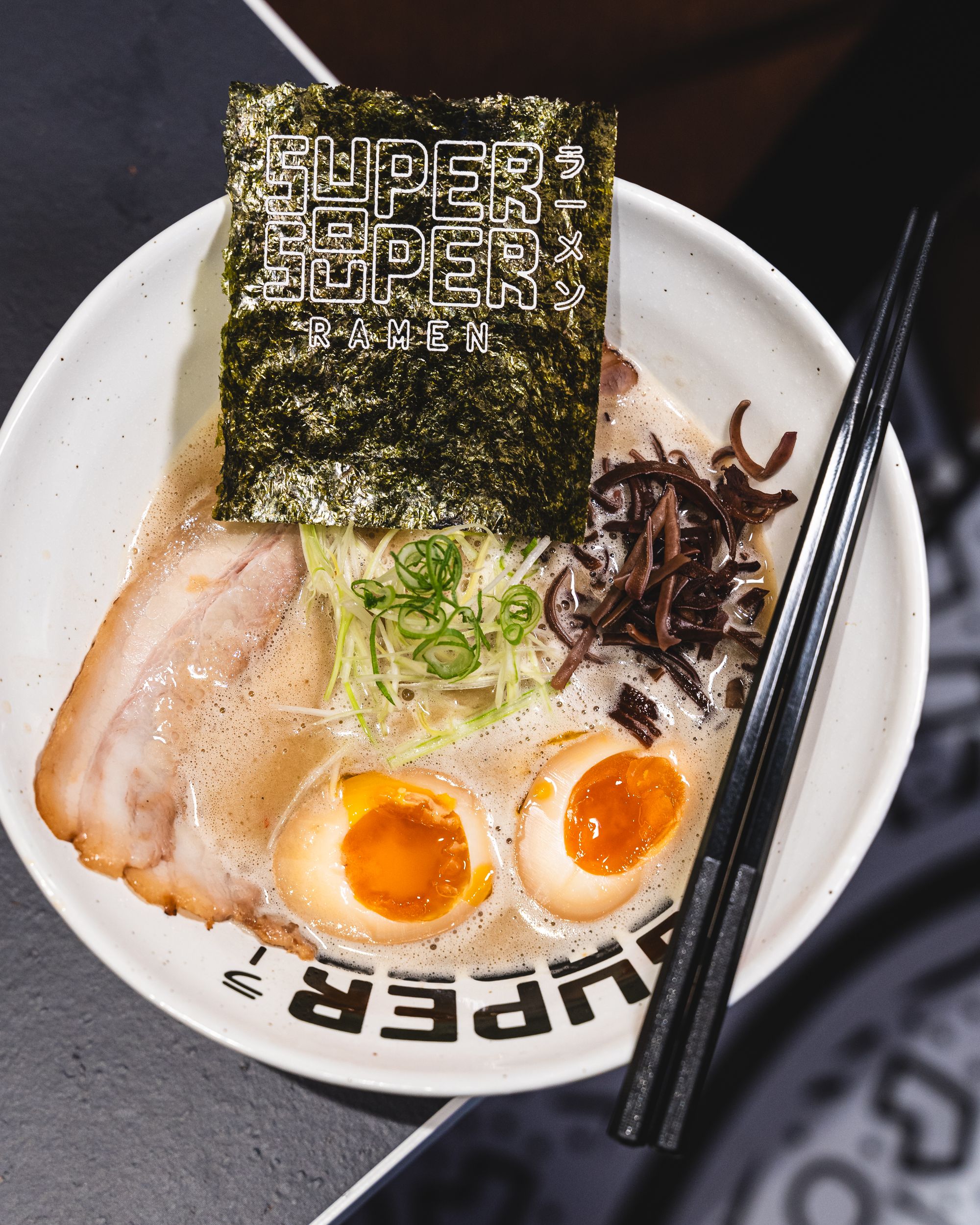 Top down shot of ramen with chashu, egg, seaweed, nori and chopsticks resting on the bowl