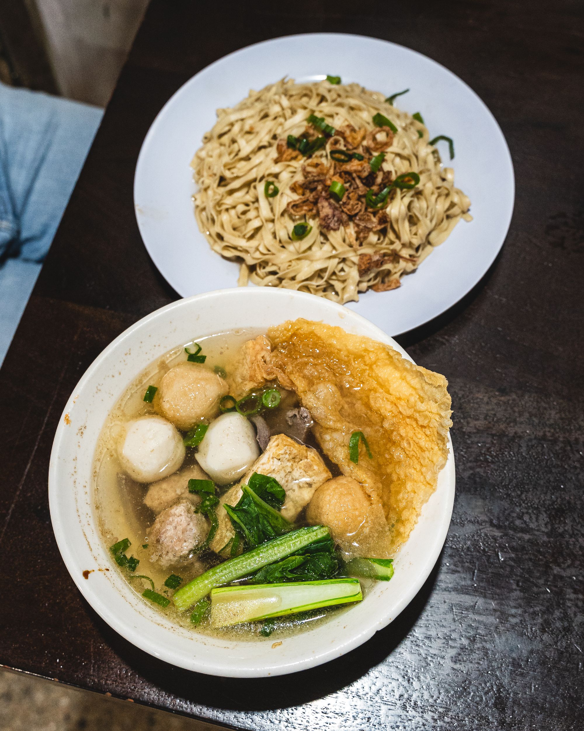 Top down shot of noodles in a bowl and another bowl with tofu, vegetables, fishballs and broth