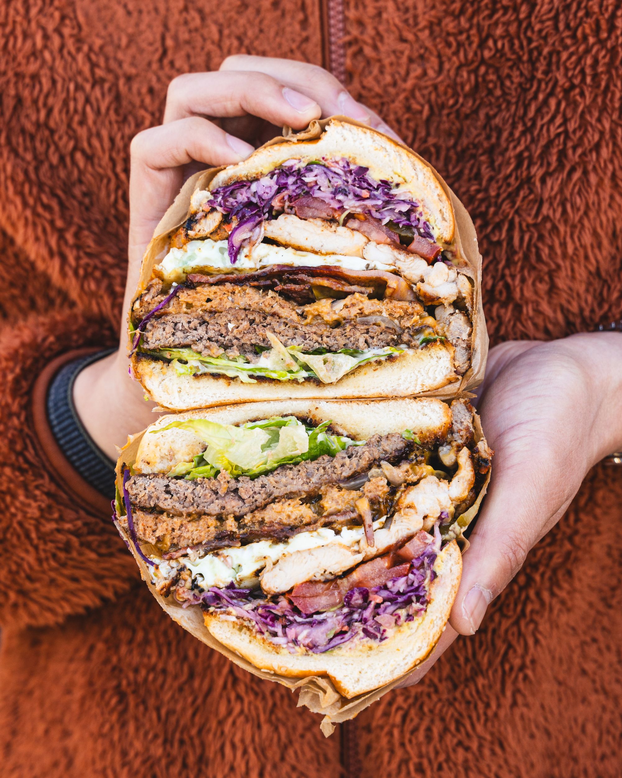 Hand holding a burger with lettuce, beef patty, grilled chicken, purple raddish and cheese