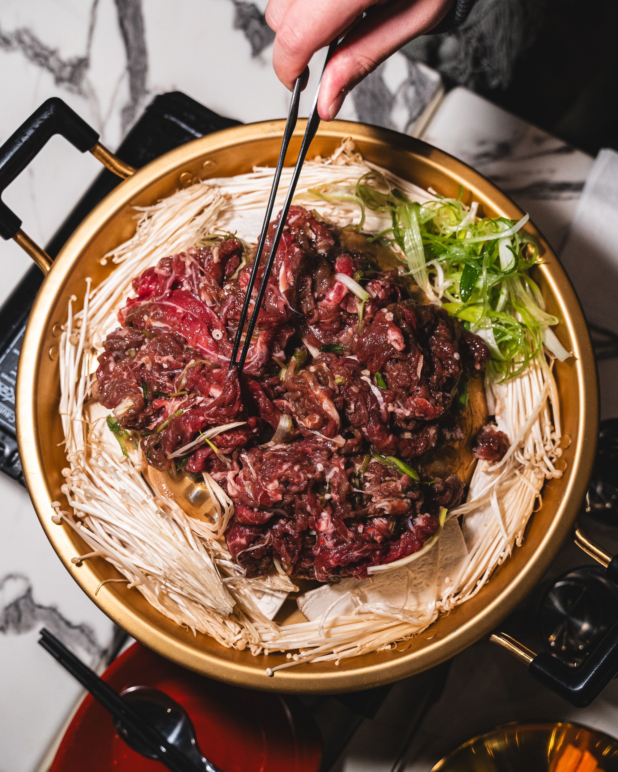 Top down shot of raw beef on a metal circular pan with enoki mushroom on side